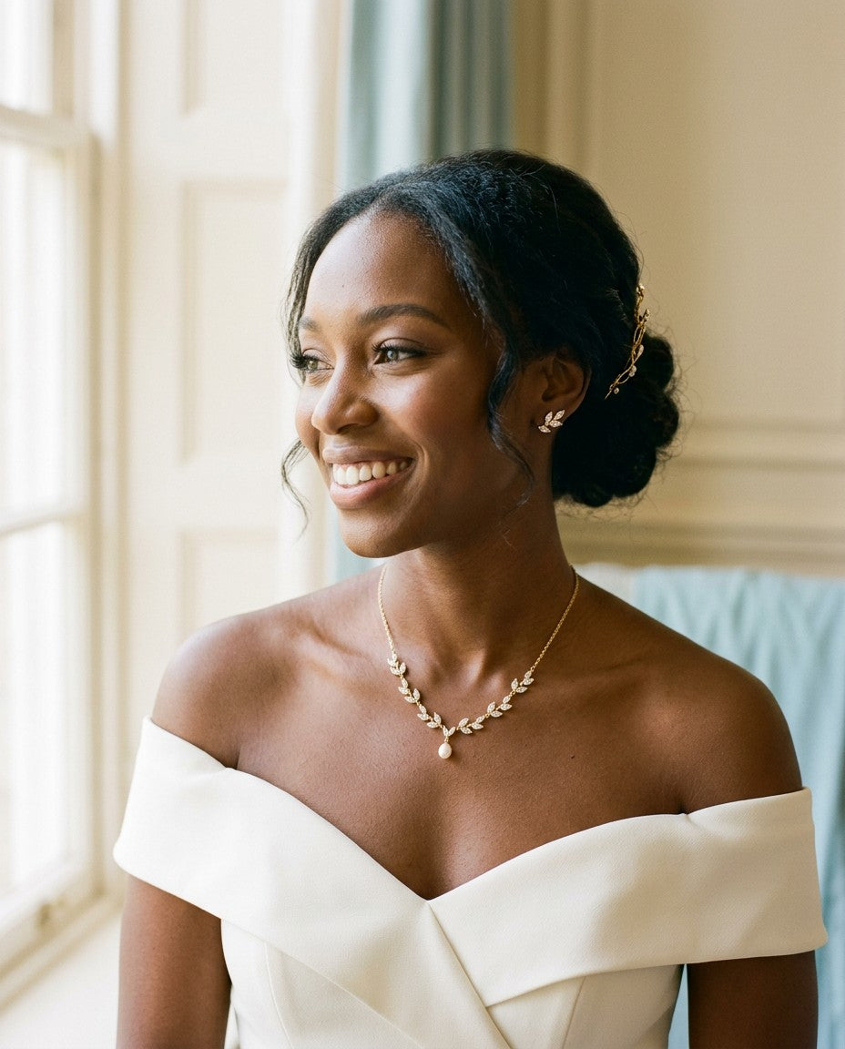 Smiling bride with an updo in an ivory off-shoulder gown wearing a gold CZ leaf necklace with a pearl drop