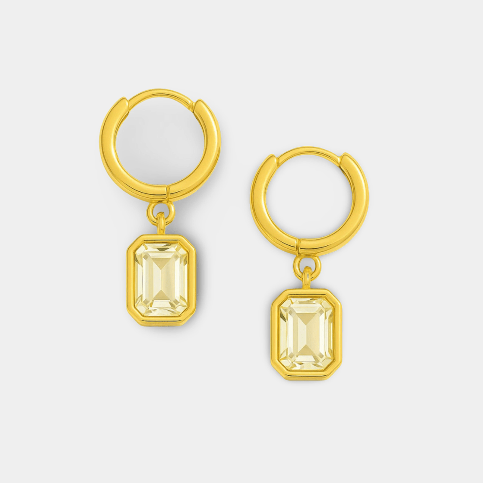 Close-up of gold huggie hoop earrings showing faceted emerald-cut zircon charms and tarnish-free gold PVD coating