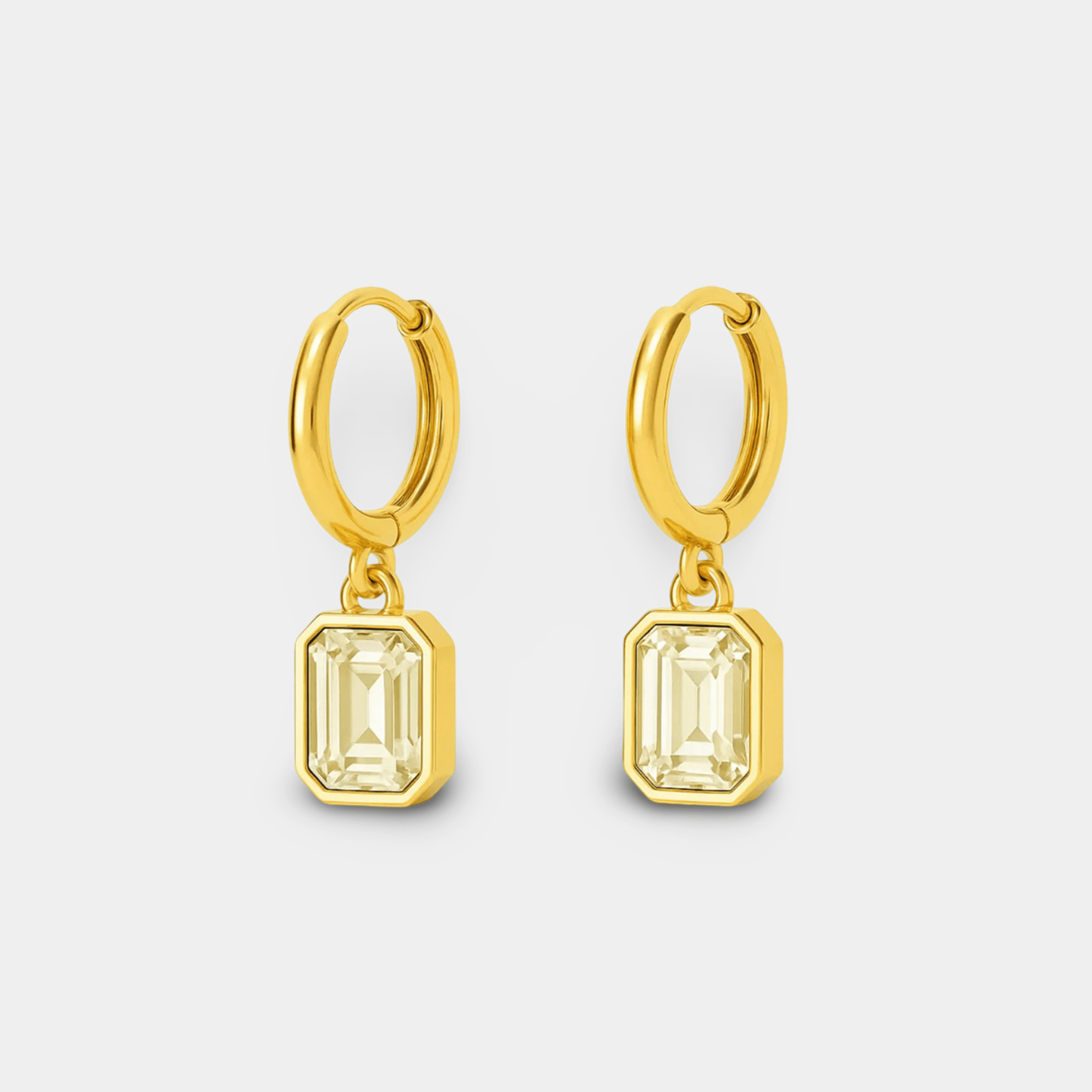Front view of a pair of gold huggie hoop earrings with emerald-cut zircon dangle charms, non-tarnish jewelry on white background