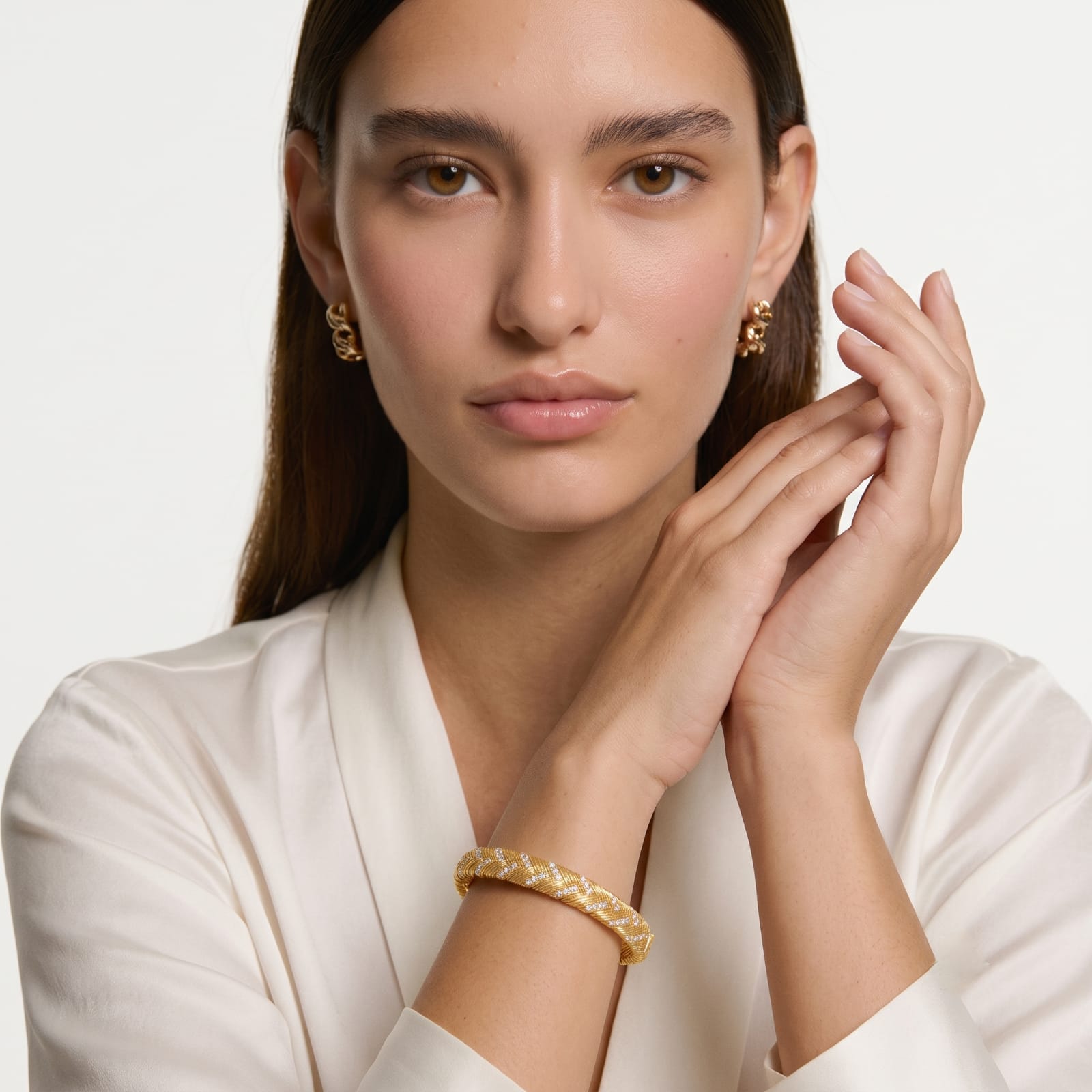Model wearing braided gold bangle bracelet and gold earrings with a white blazer