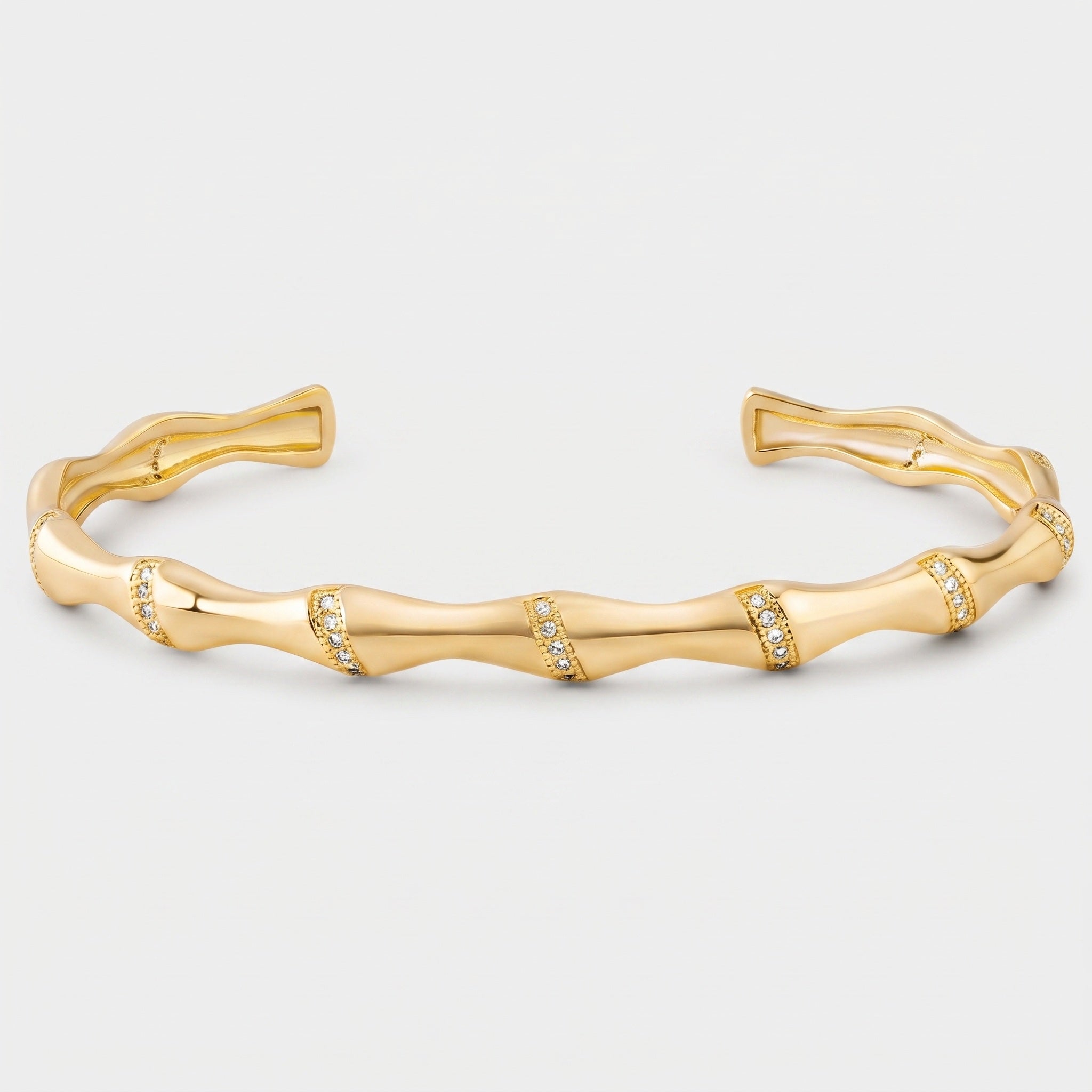 A gold cuff bracelet designed to look like a wavy bamboo stalk, featuring small clear pavé-set stones along the segmented center, shown on a light gray background.