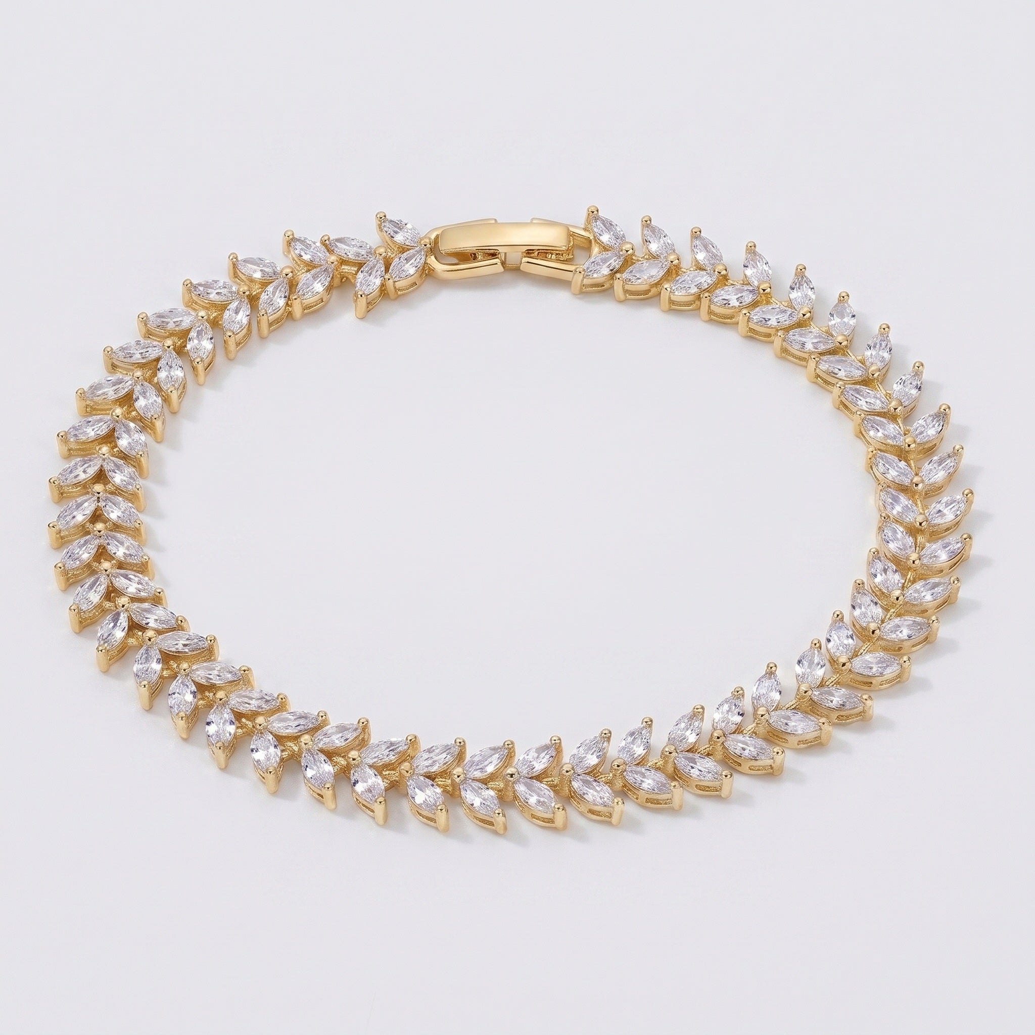 A gold tennis bracelet featuring marquise-cut clear crystals set in a leaf pattern, displayed on a clean light gray background.