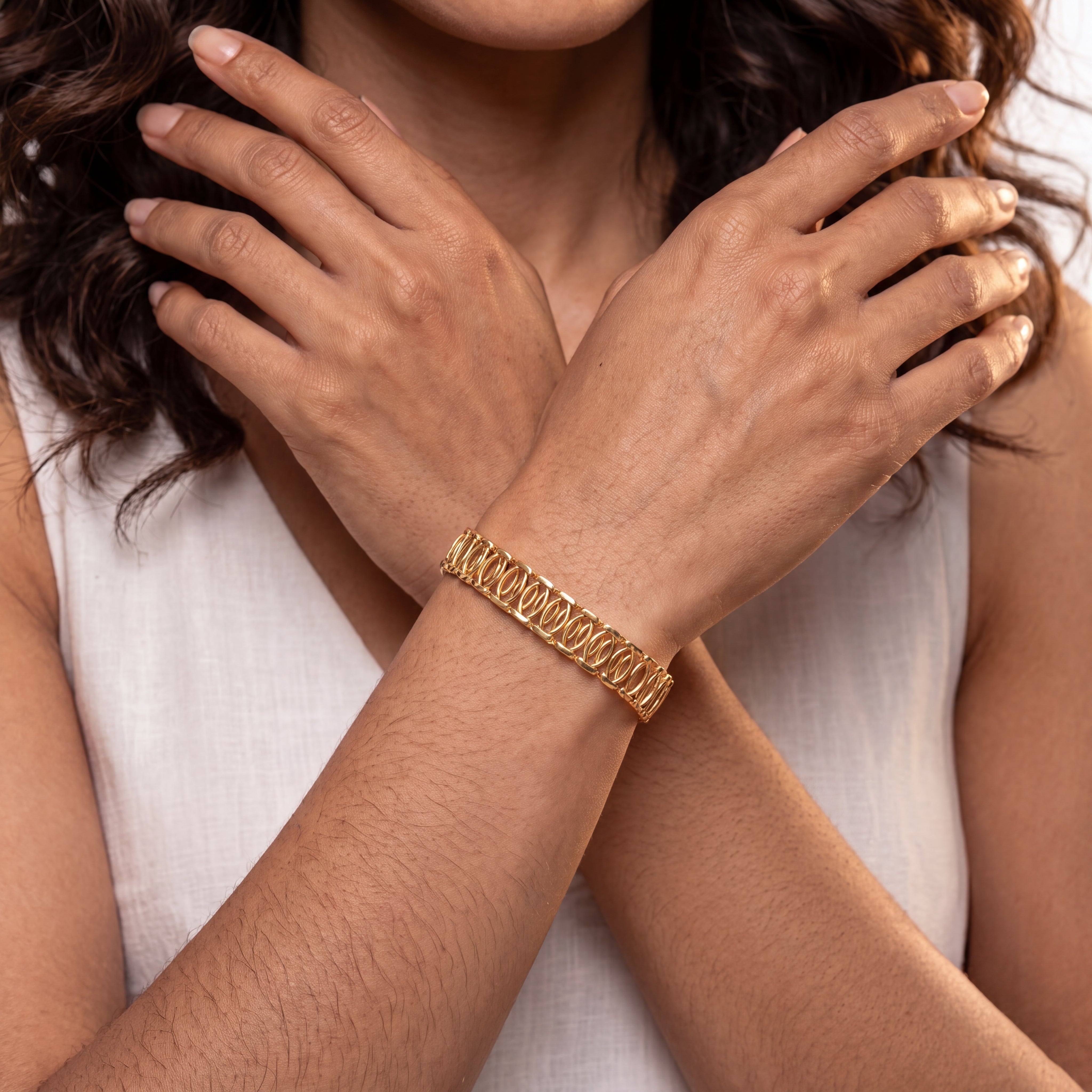 A close-up of a woman wearing a textured gold chain bracelet on her wrist, with her hands crossed over her chest.