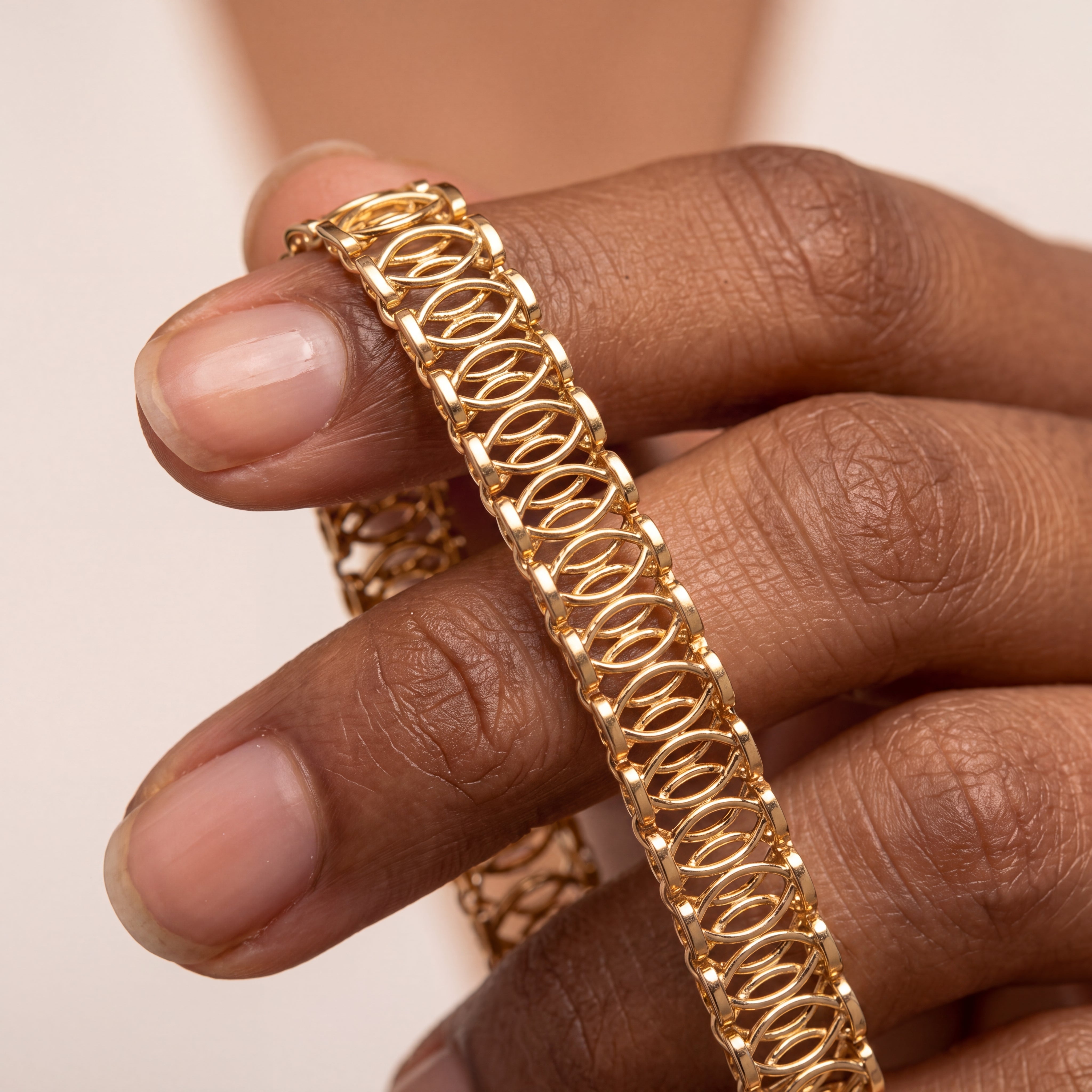 A close-up of a hand holding a gold bangle bracelet with an intricate openwork geometric pattern.