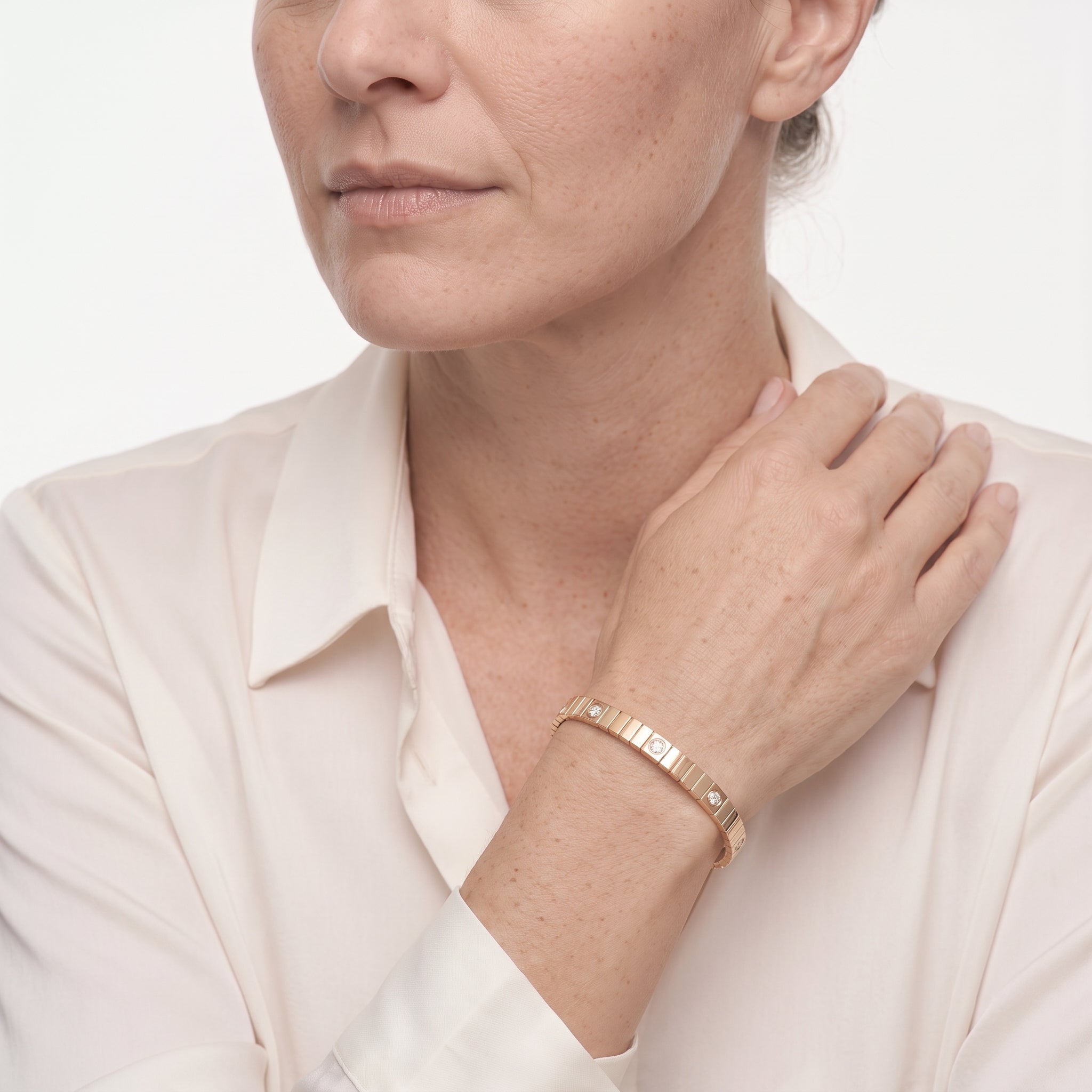 Close view of the gold plated ribbed bangle bracelet on a woman's wrist with a cream silk shirt
