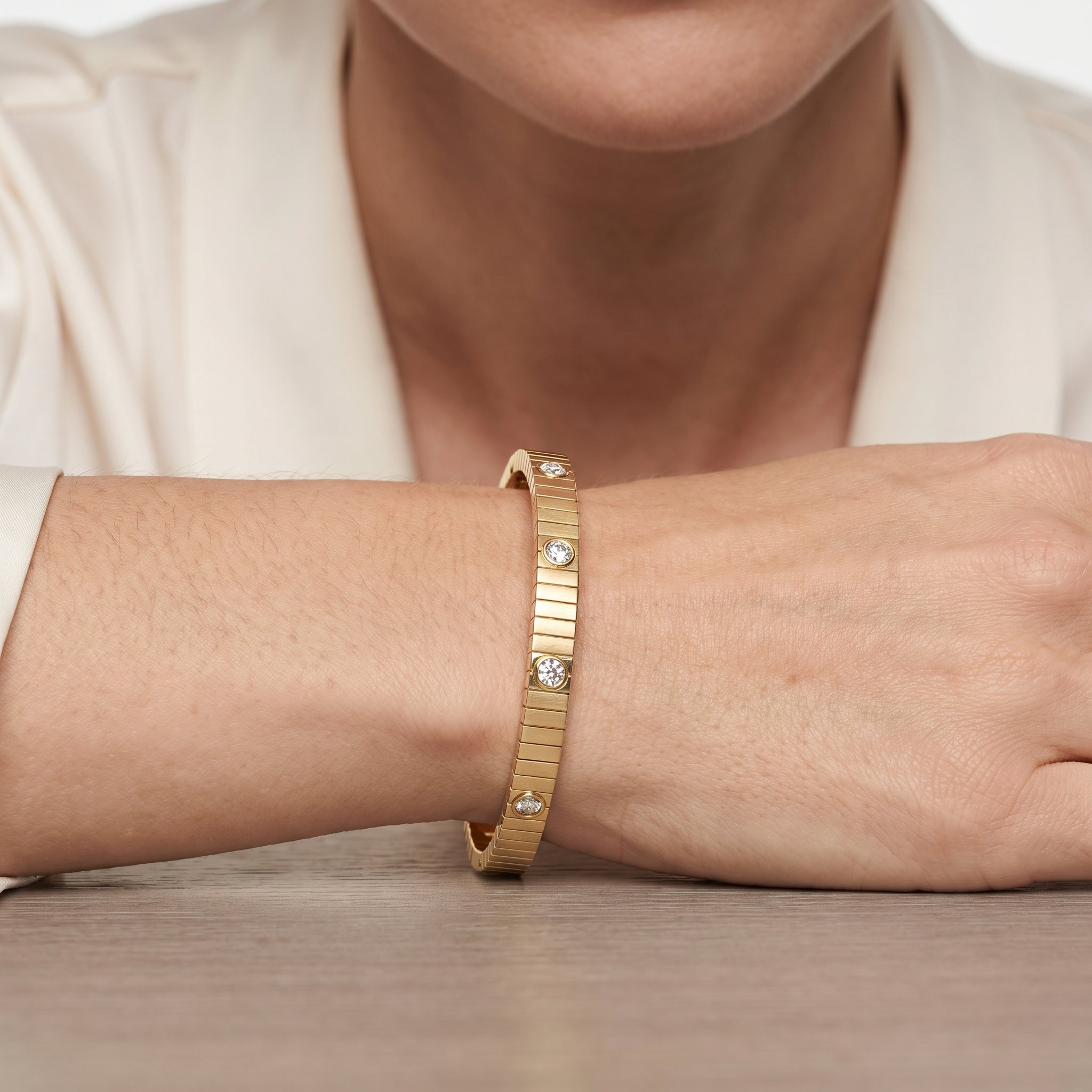 Gold plated ribbed bangle bracelet with cubic zirconia stones shown on a wrist resting on a wooden table