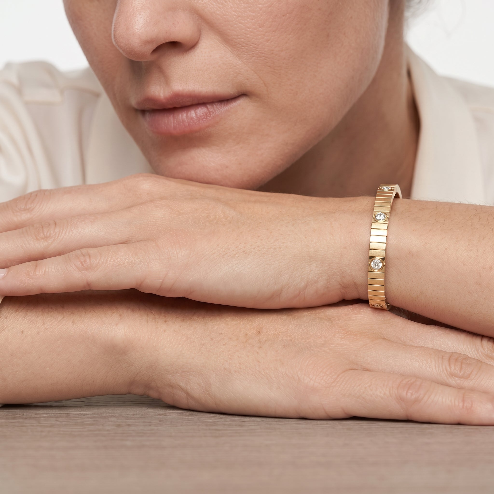 Woman in a cream blouse wearing the 14K gold plated ribbed CZ bangle bracelet with her hand at her collarbone