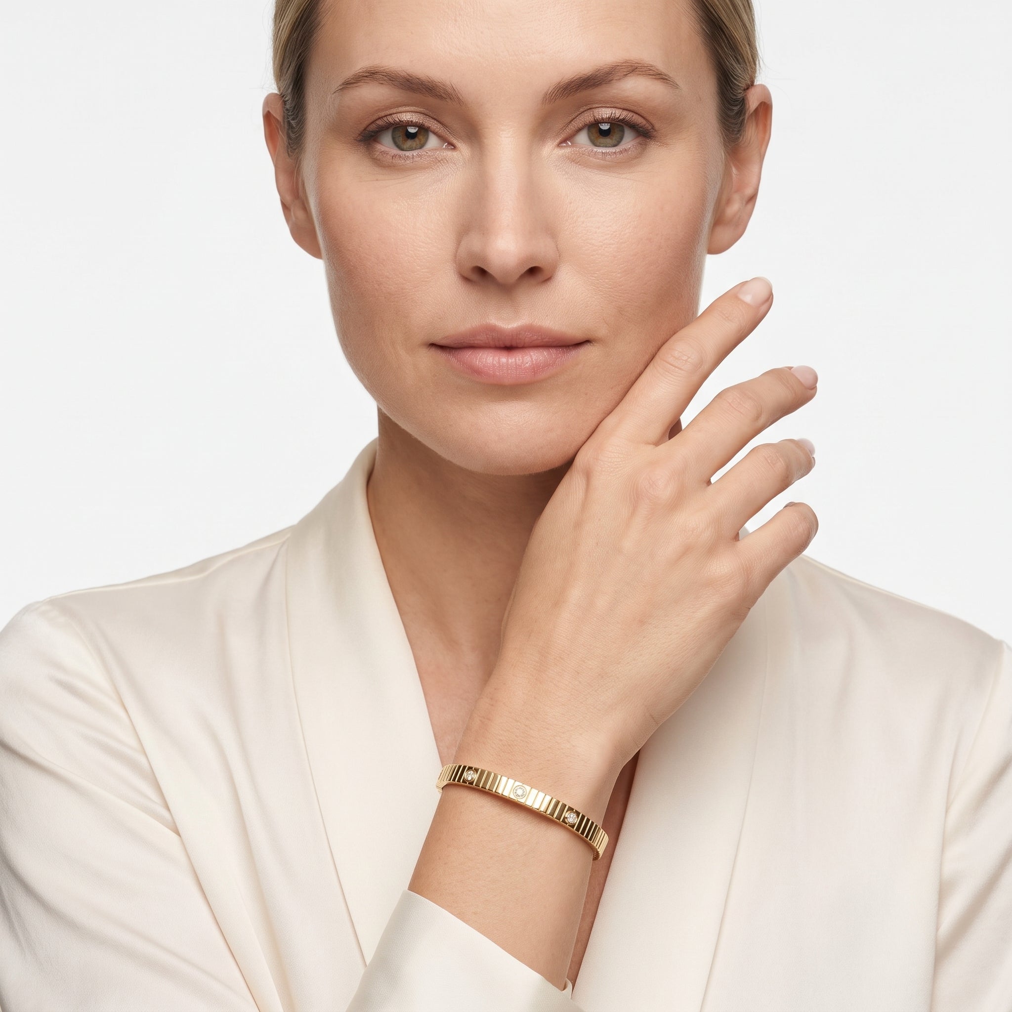 Woman in a cream blazer wearing the ribbed gold plated CZ bangle bracelet with her hand to her cheek