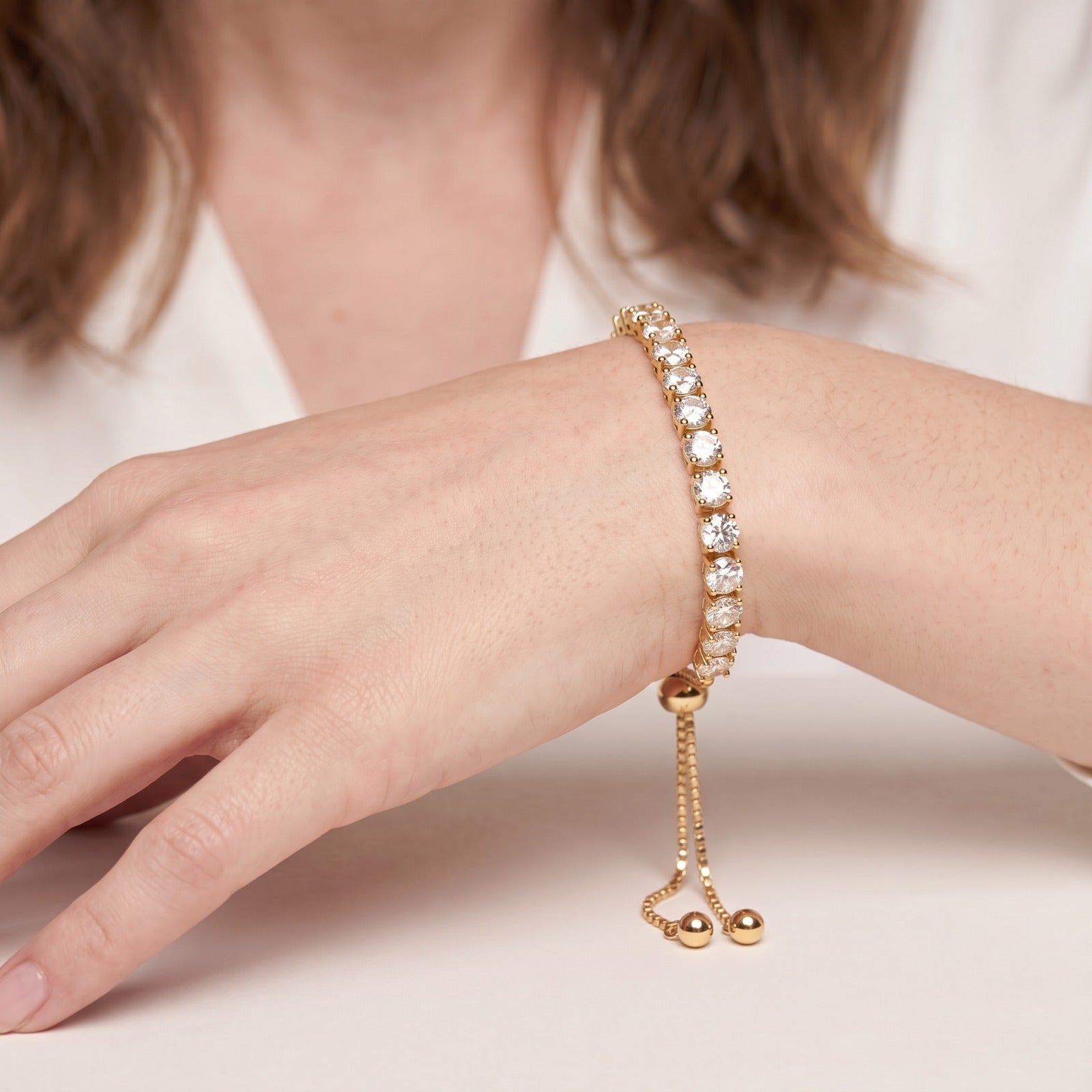 Gold plated CZ tennis bracelet on a woman's wrist showing the slider clasp and two hanging gold ball ends