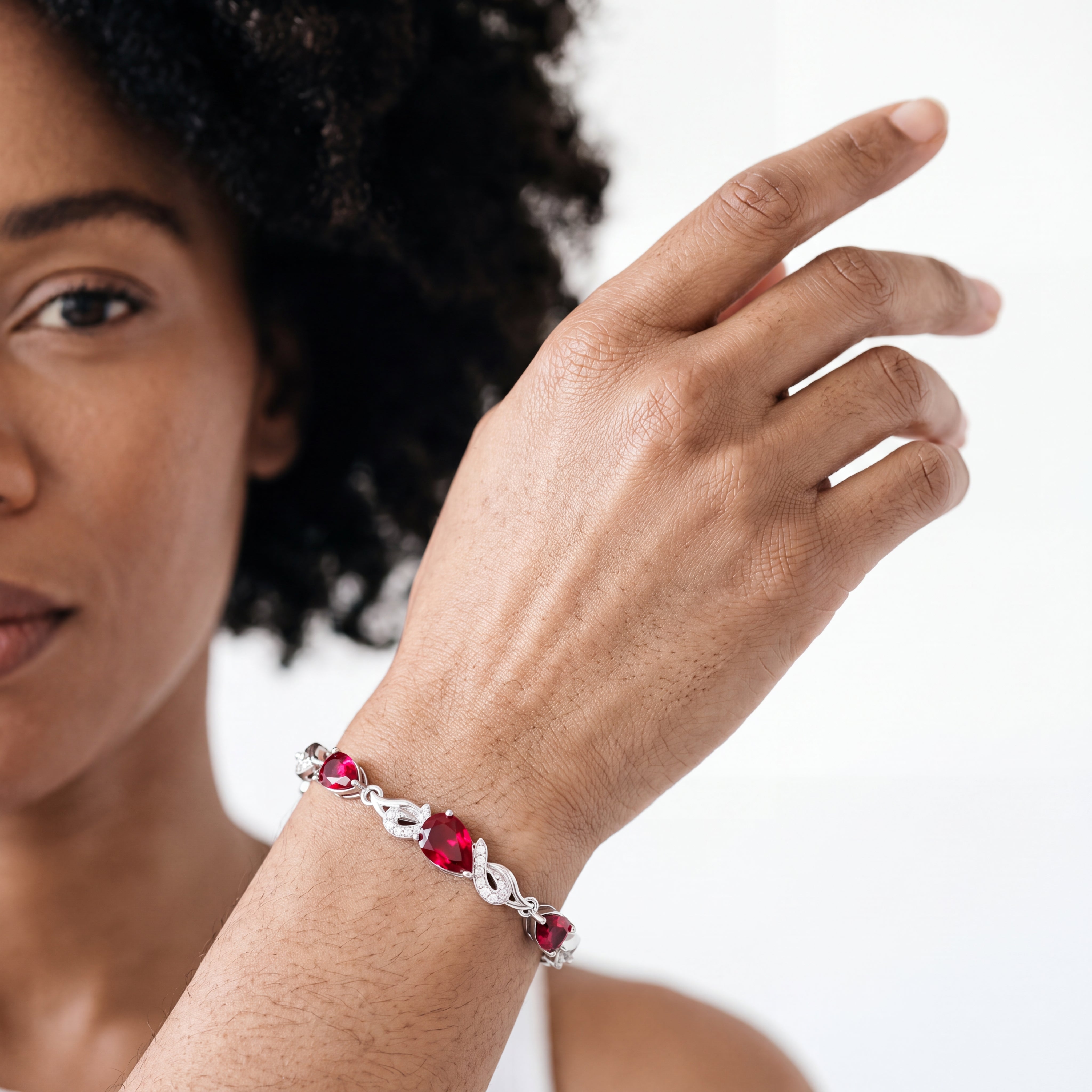 Close-up of a woman wearing the ruby bracelet on her raised wrist, showing the deep red teardrop stones.