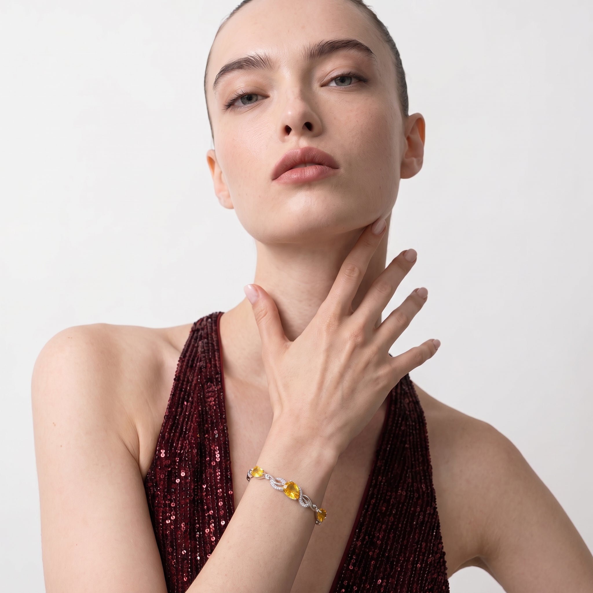 Close-up of a woman wearing the citrine teardrop bracelet on her wrist while touching her neck, wearing a burgundy dress.