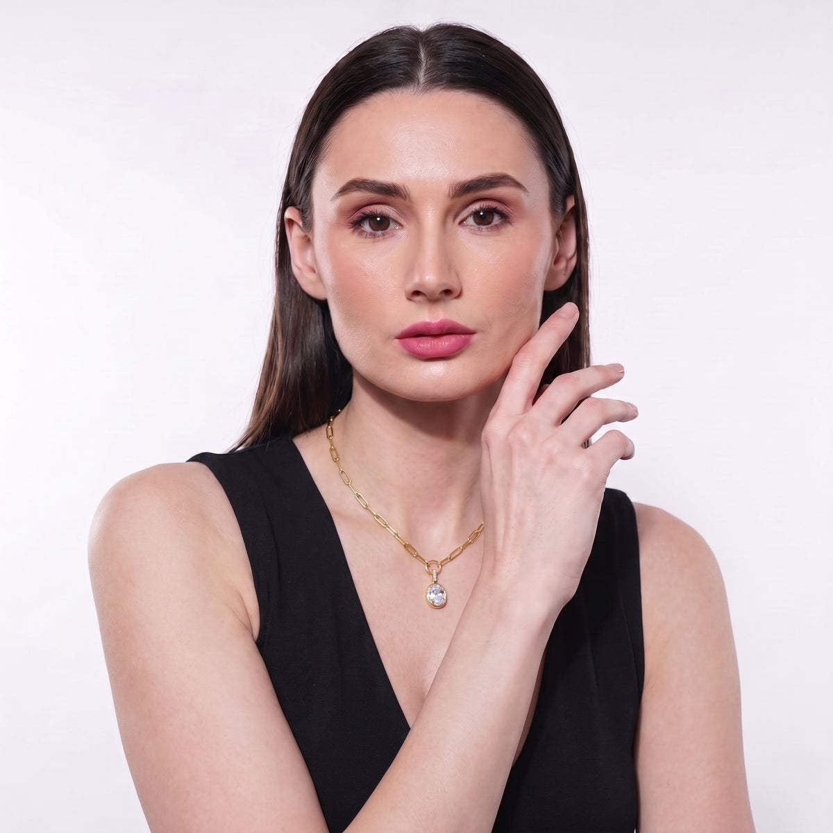 Woman in a black top wearing a dainty gold paperclip necklace with an oval CZ solitaire pendant