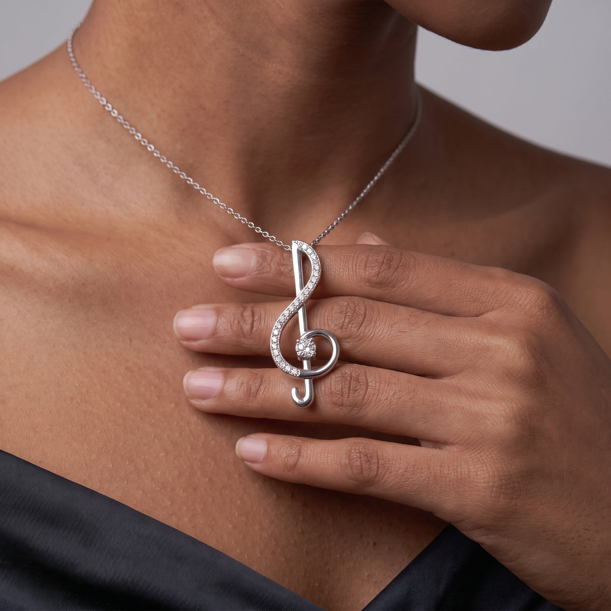 Close-up of a hand holding a moissanite treble clef pendant at the collarbone