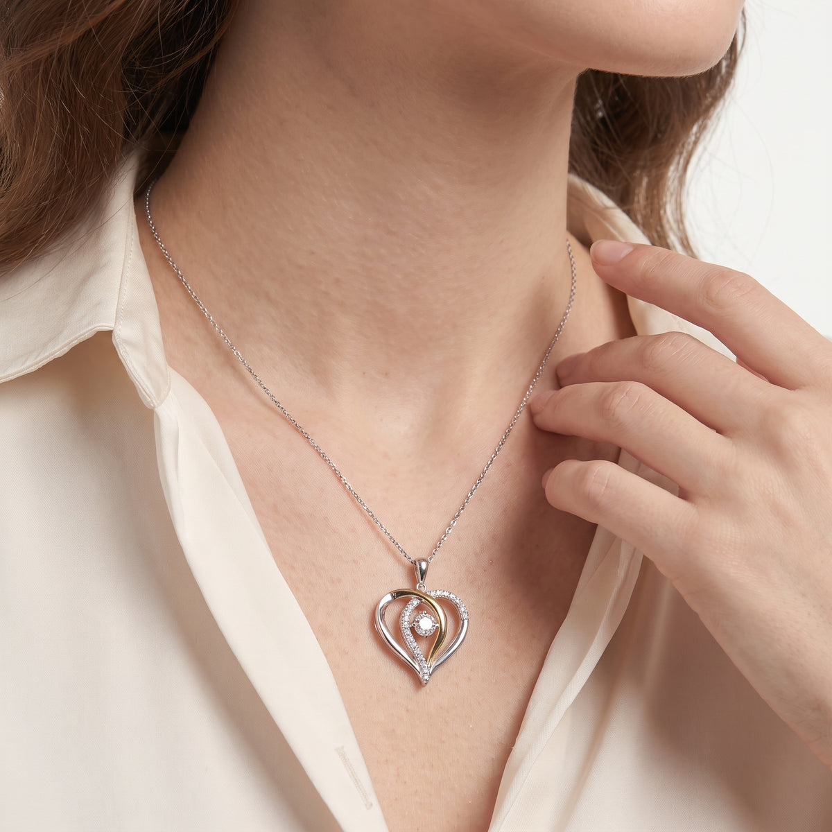 Woman in a cream blouse wearing a dancing moissanite heart necklace on a silver chain