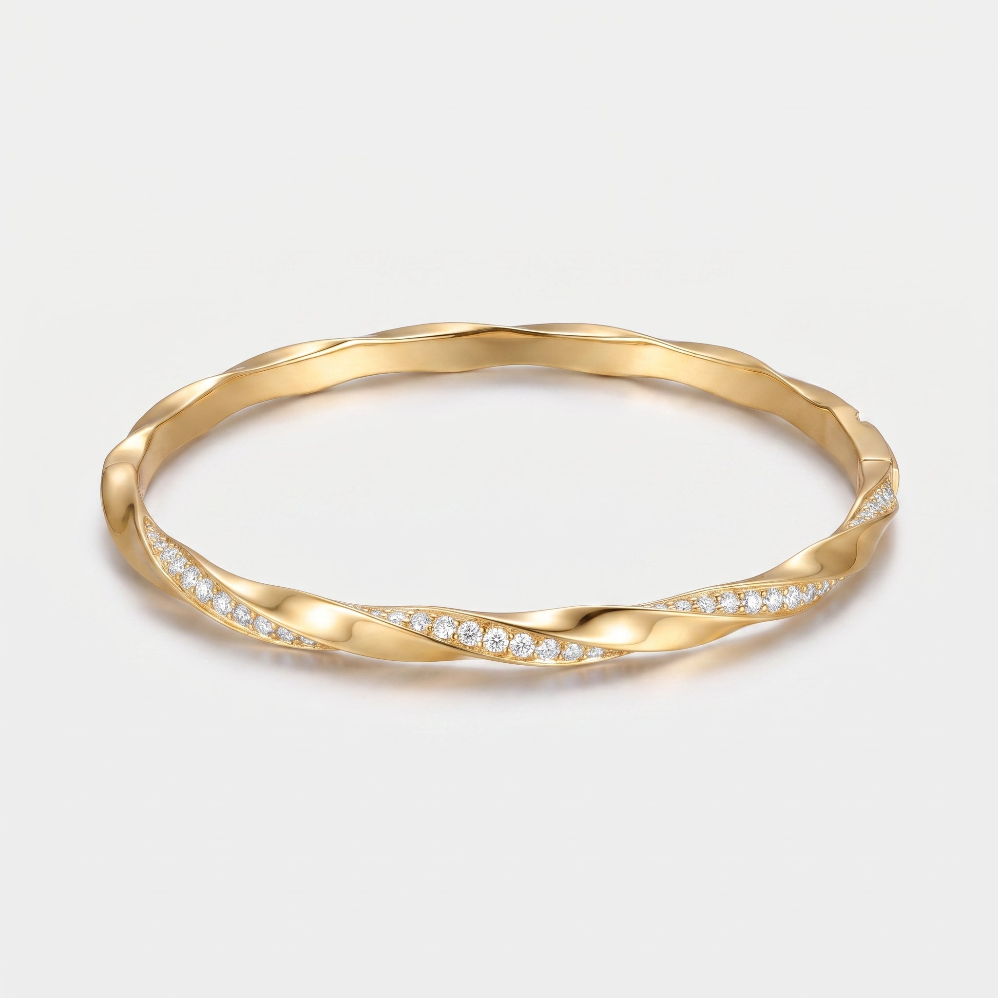 A twisted gold bangle bracelet with a row of small clear pavé stones along one side, shown on a clean light gray background.