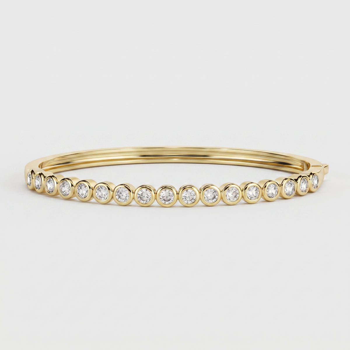 A gold bangle bracelet featuring a row of round-cut clear gemstones in bezel settings, photographed on a clean light gray background.