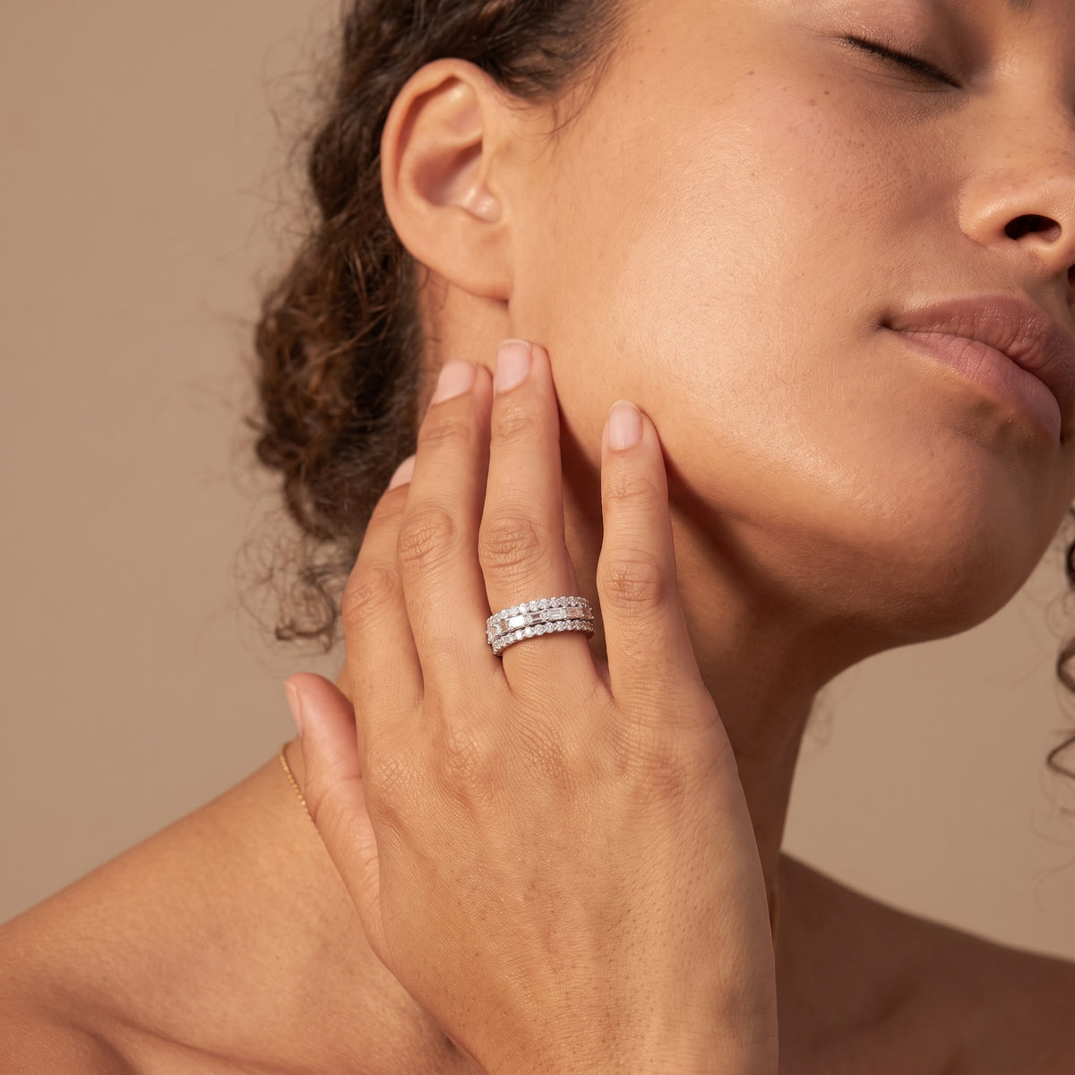 Woman with eyes closed and hand on her cheek wearing a sparkling three row wedding band