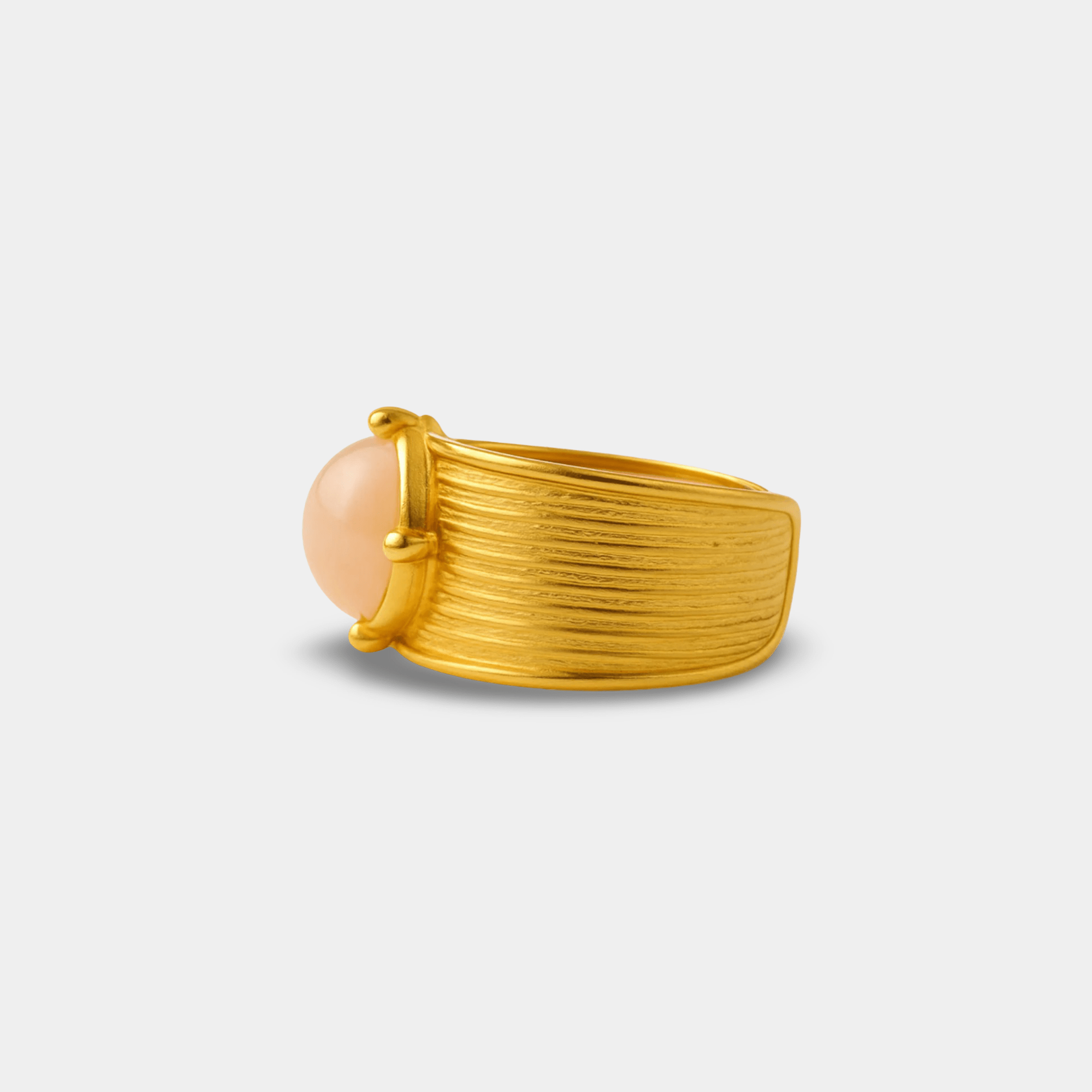 Close-up of the ribbed gold texture and prong-set blush gemstone cabochon on the dynasty cuff ring