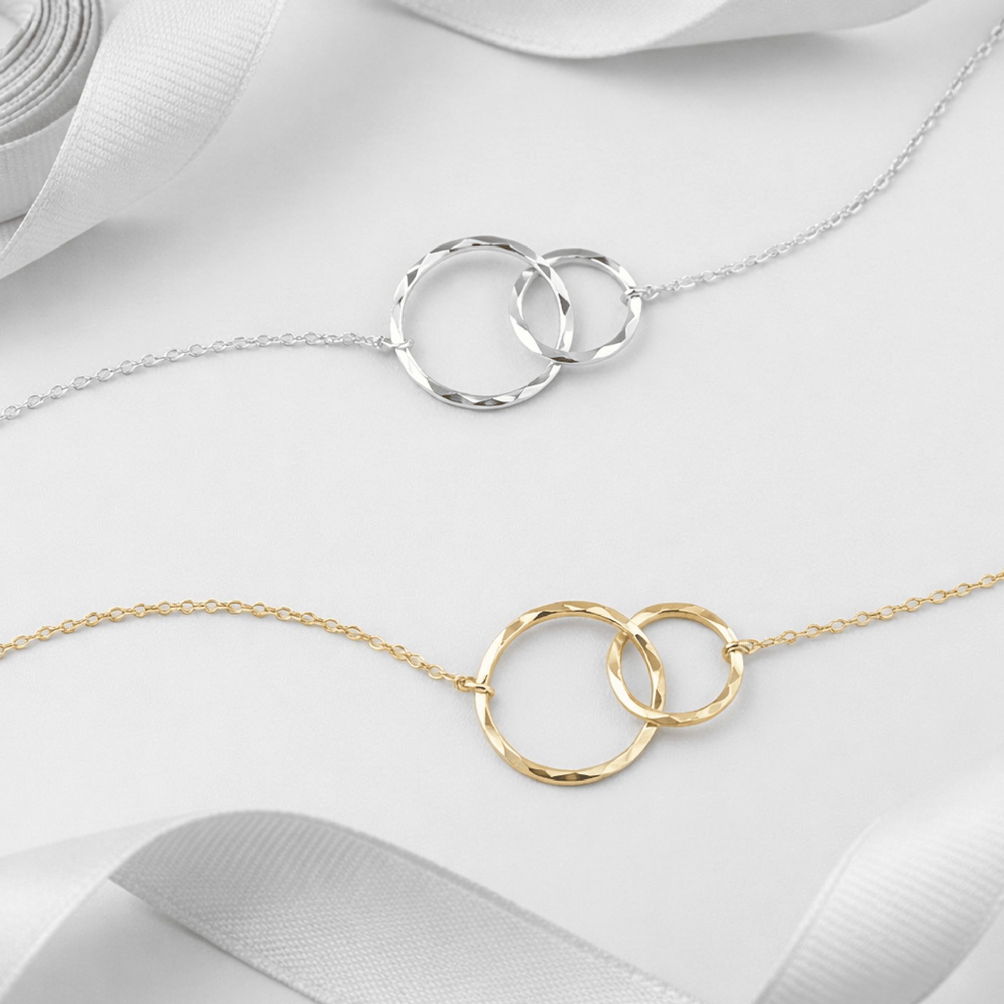 Silver and gold maid of honor necklaces with interlocking circles pendants displayed side by side with white ribbon