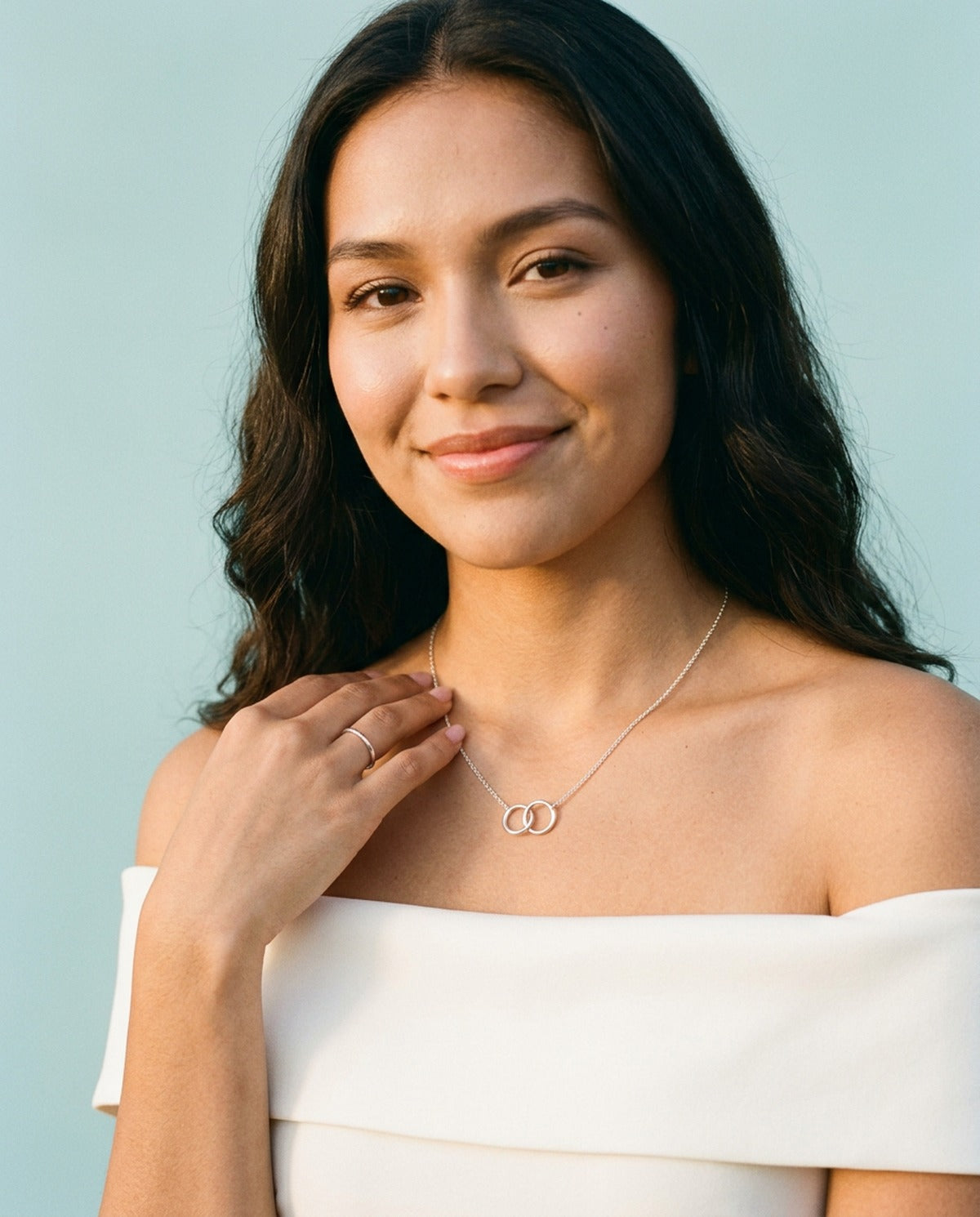 Woman in an ivory off-shoulder dress wearing a silver interlocking circles necklace, an anniversary gift idea