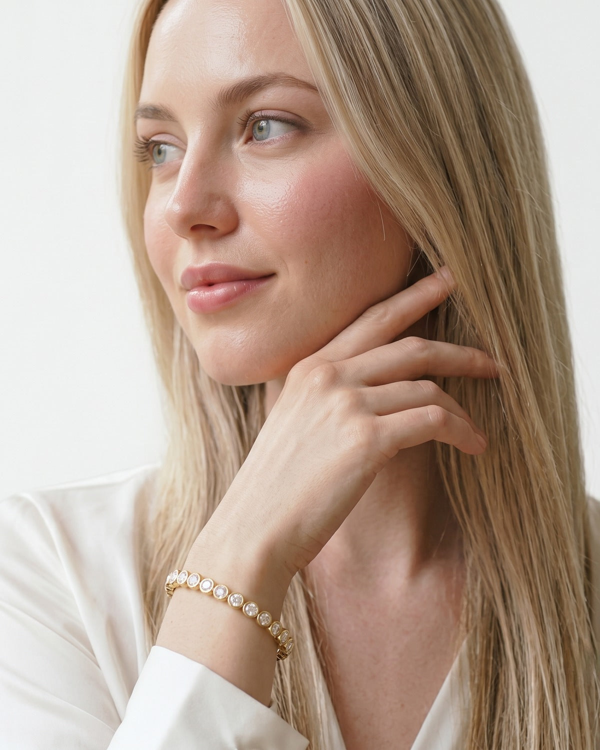 Woman in a white blouse with her hand at her jaw, wearing a gold cubic zirconia tennis bracelet