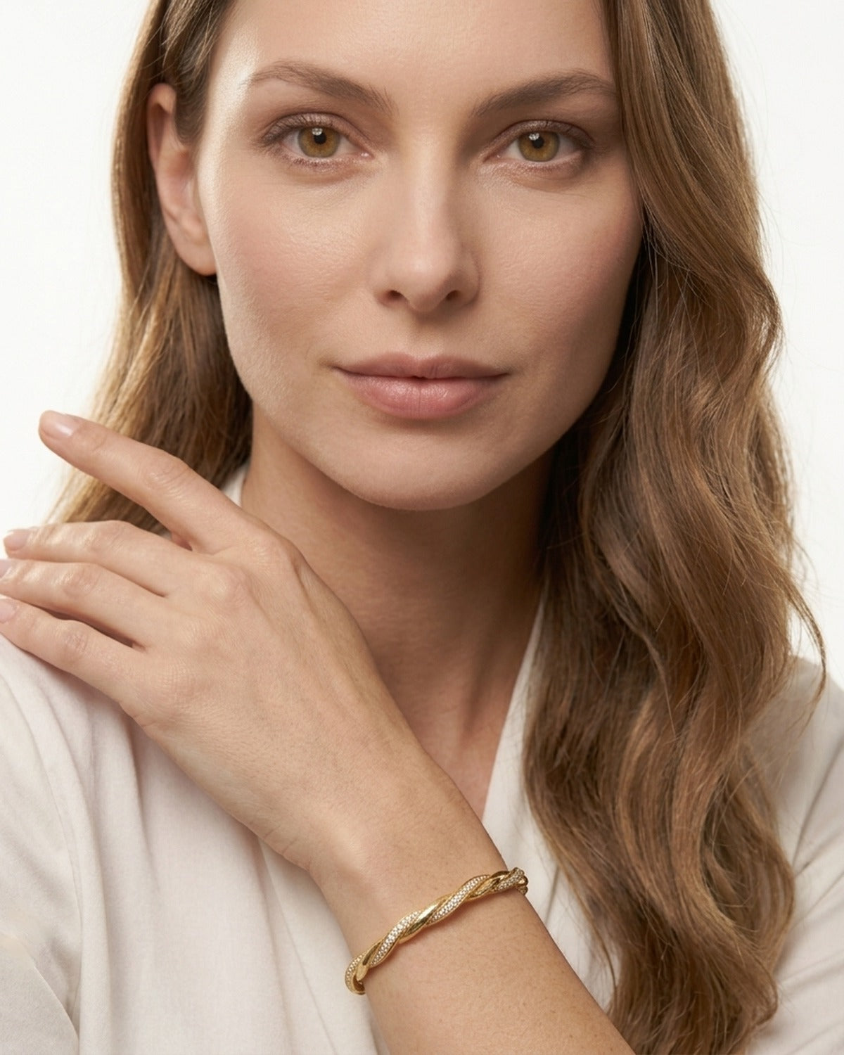 Woman in an ivory blouse with her hand at her shoulder, wearing a twisted gold bangle bracelet