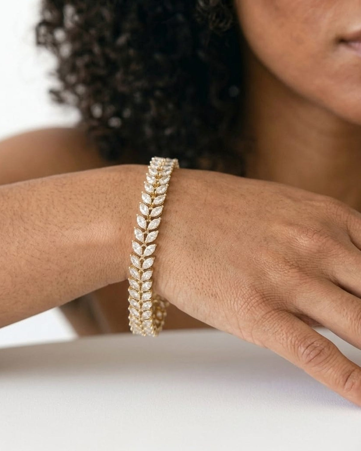 Woman resting her wrist on a white table, wearing a gold marquise leaf tennis bracelet