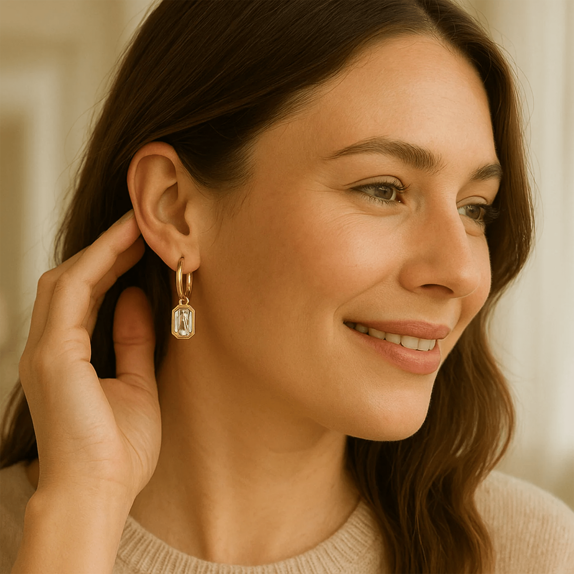 Smiling woman modeling gold huggie hoop earrings with emerald-cut zircon charms, lightweight everyday charm hoops