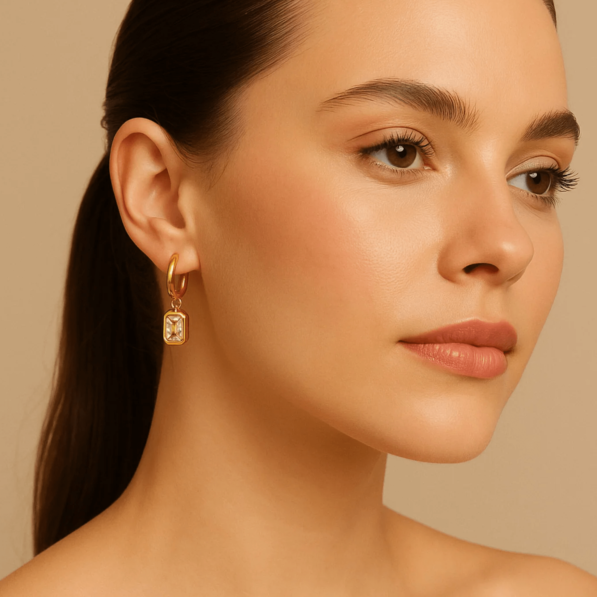 Woman wearing a hypoallergenic gold huggie hoop earring with an emerald-cut zircon dangle charm for everyday wear
