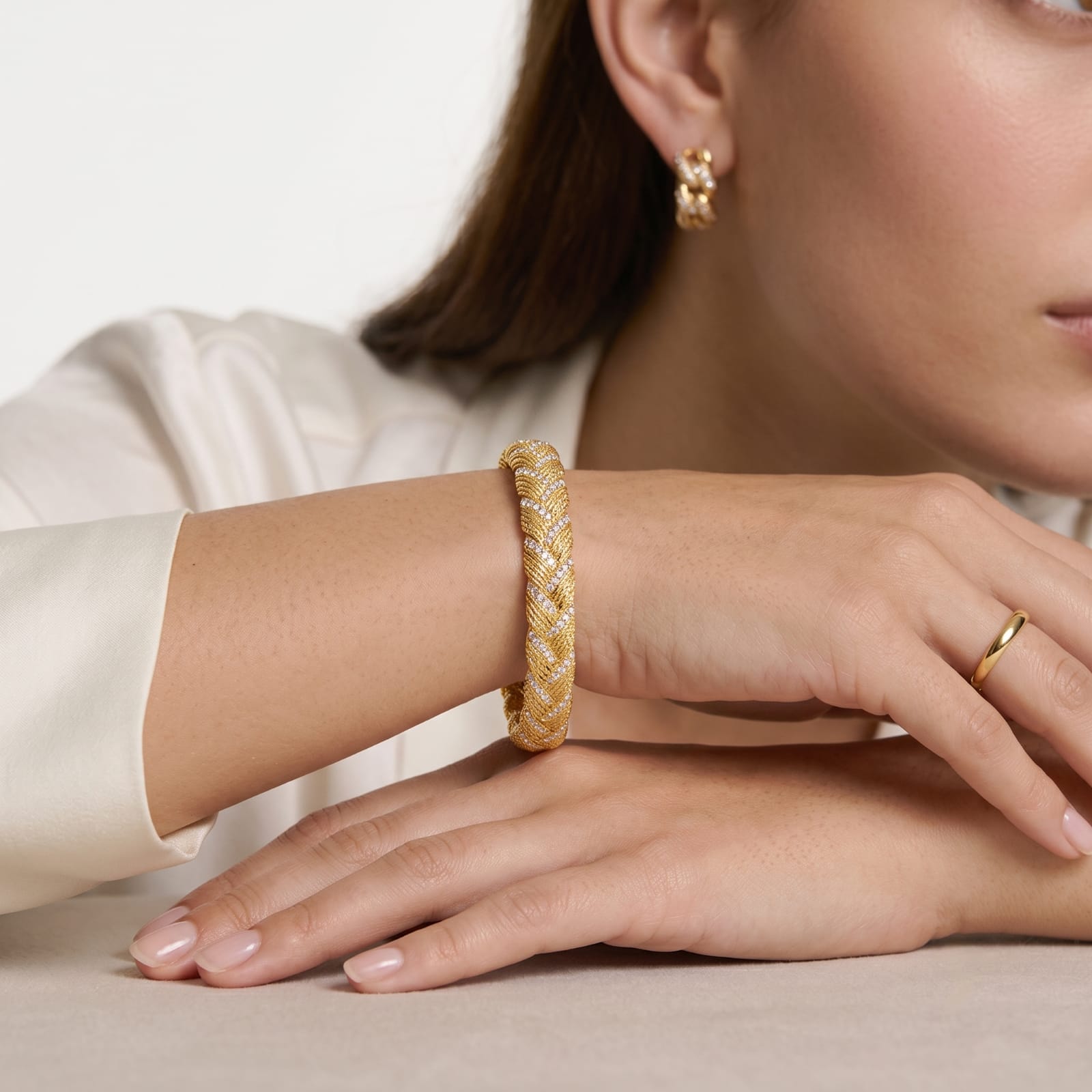 18K gold plated braided bangle bracelet worn on a wrist with gold hoop earrings