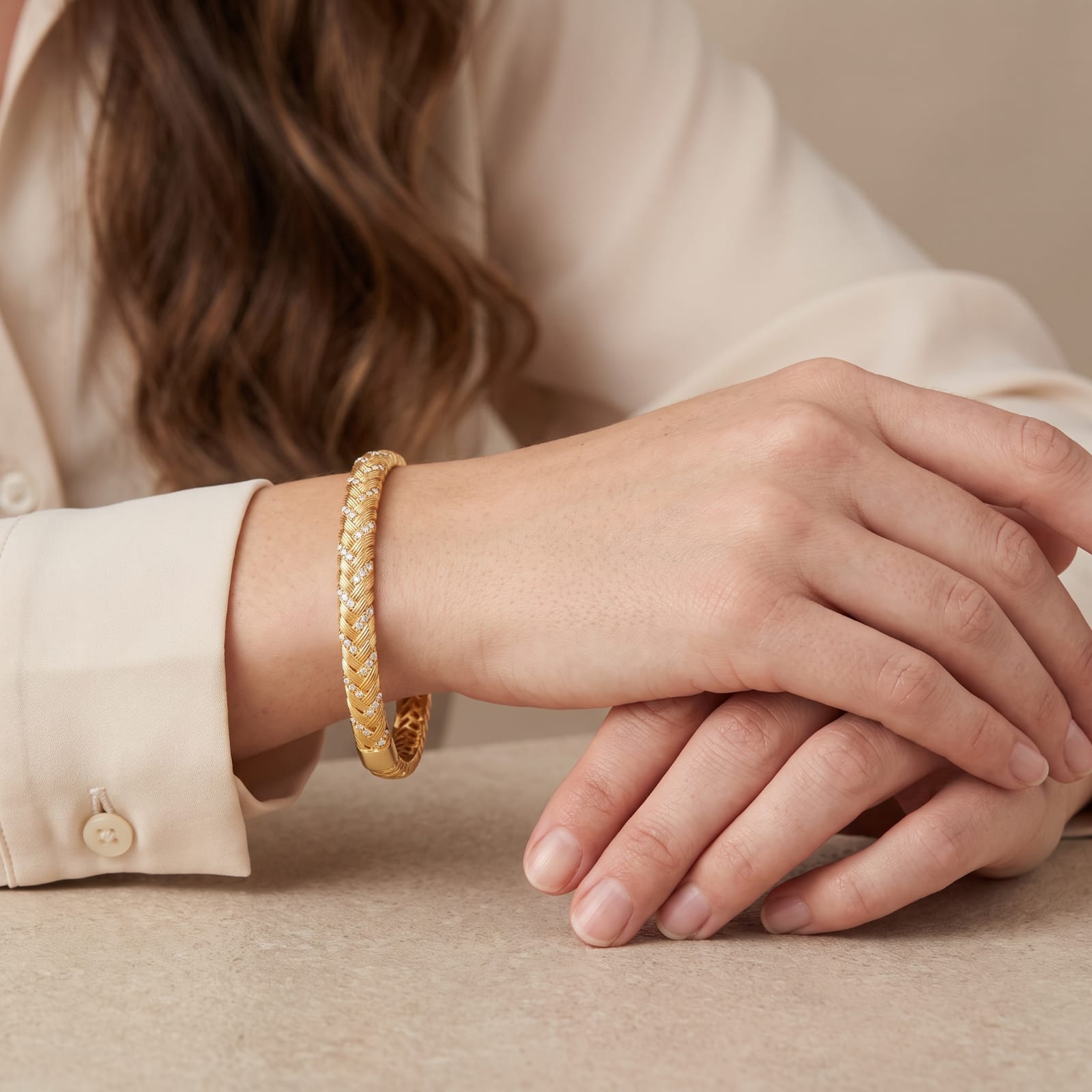 Woman wearing a braided gold bangle bracelet with a cream blouse at a table