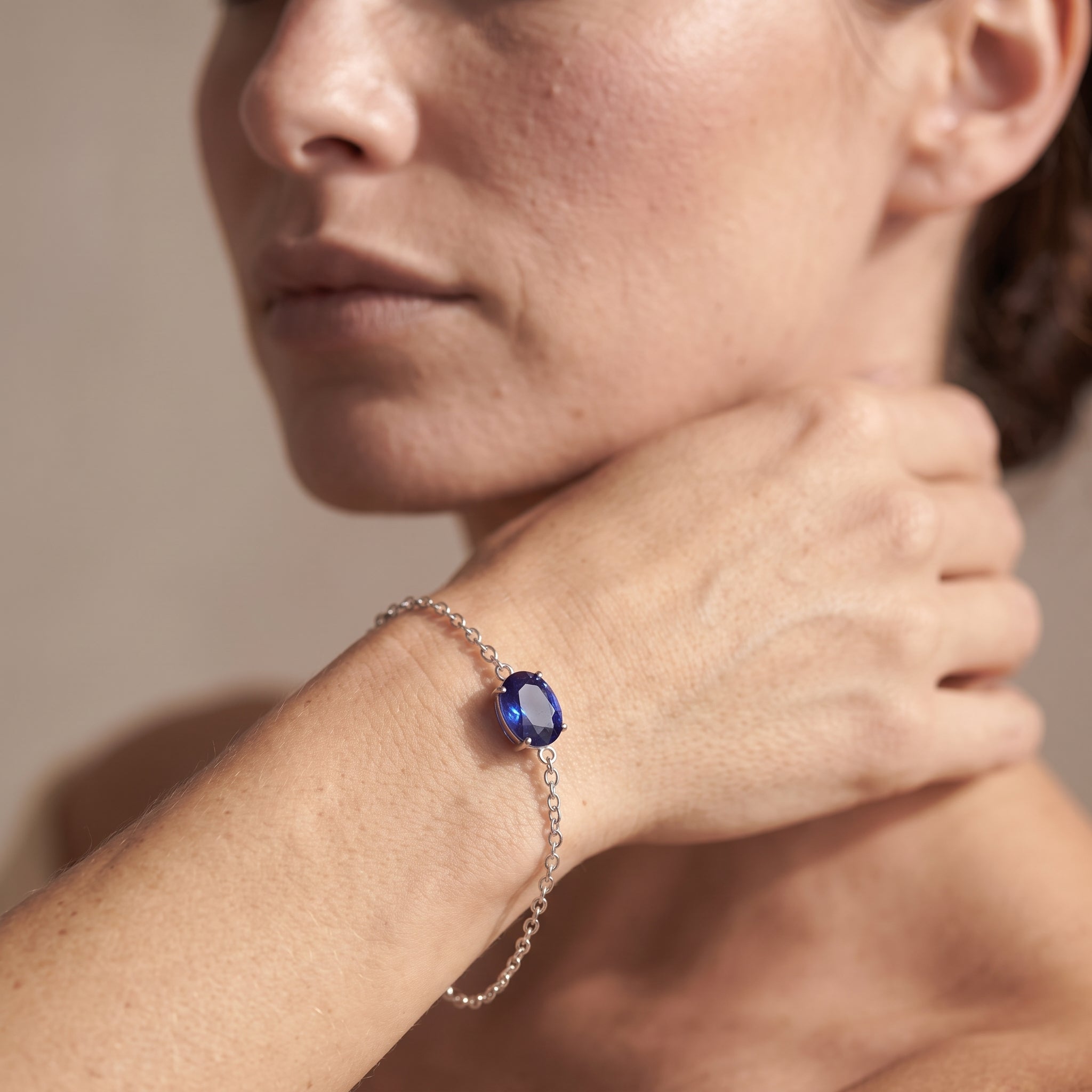 A close-up lifestyle shot of a woman wearing a delicate silver chain bracelet with a round, deep blue gemstone on her wrist.
