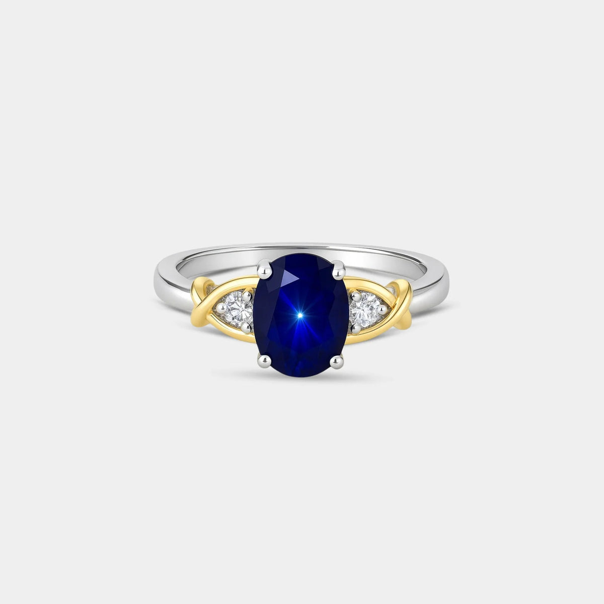 An oval-cut deep blue sapphire ring set in a two-tone silver and yellow gold band with small diamond accents on either side, shown against a light gray background.