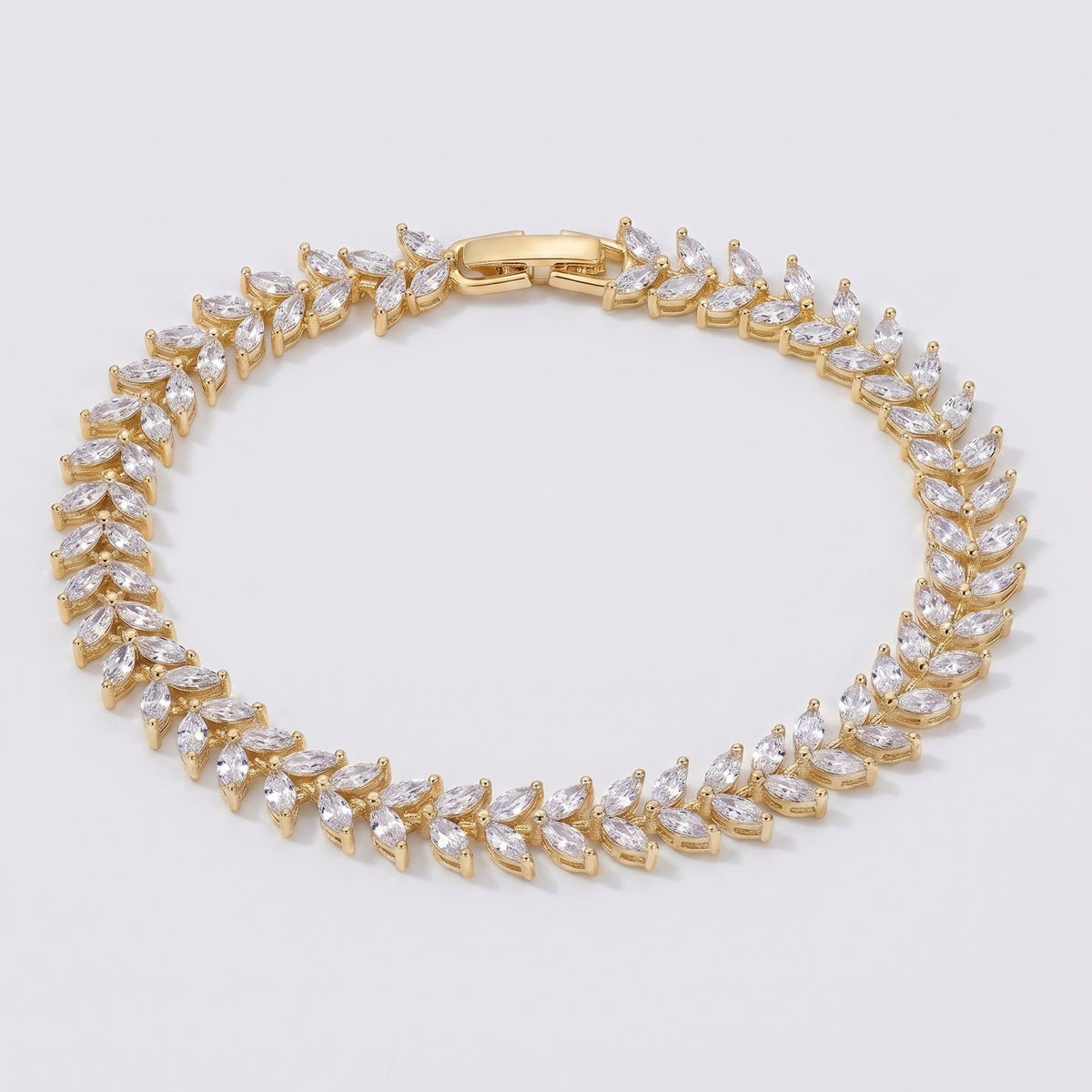 A gold tennis bracelet featuring marquise-cut clear crystals set in a leaf pattern, displayed on a clean light gray background.