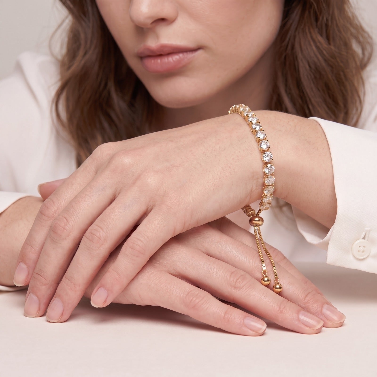 Woman in a white shirt wearing the adjustable cubic zirconia tennis bracelet with hands resting on a table