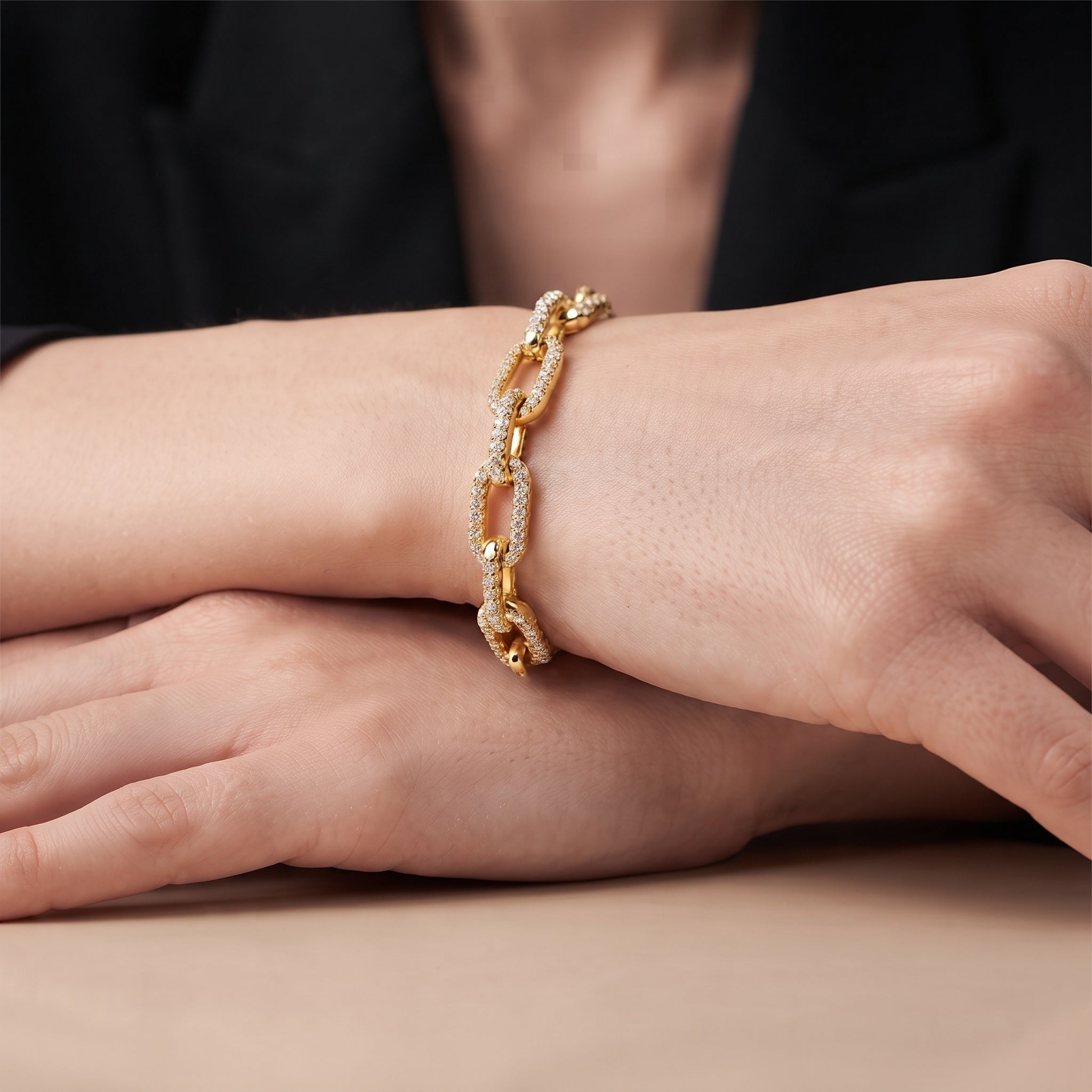 Woman wearing a gold chain link cuff bracelet with a black blazer at a table