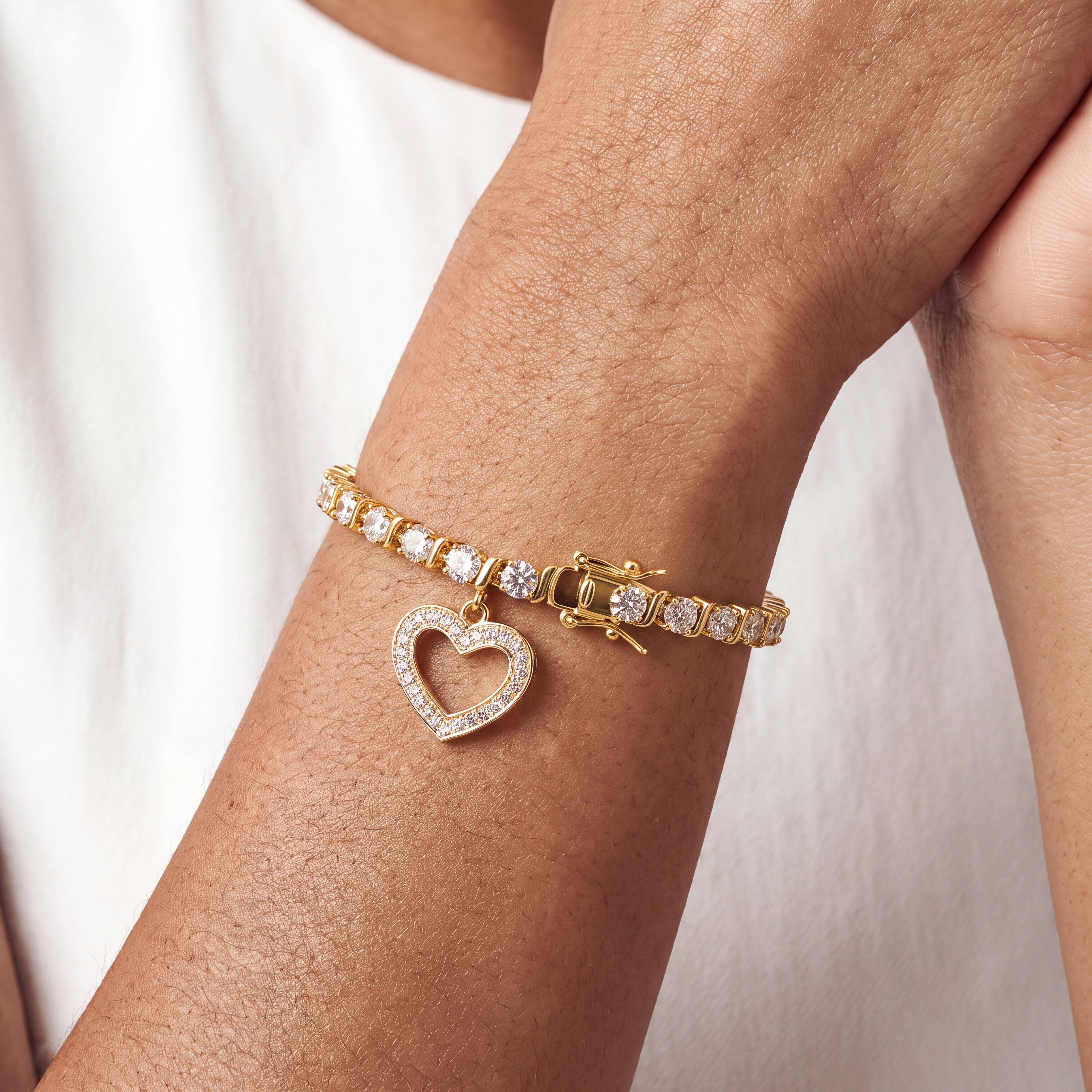 Gold heart charm tennis bracelet worn on a wrist