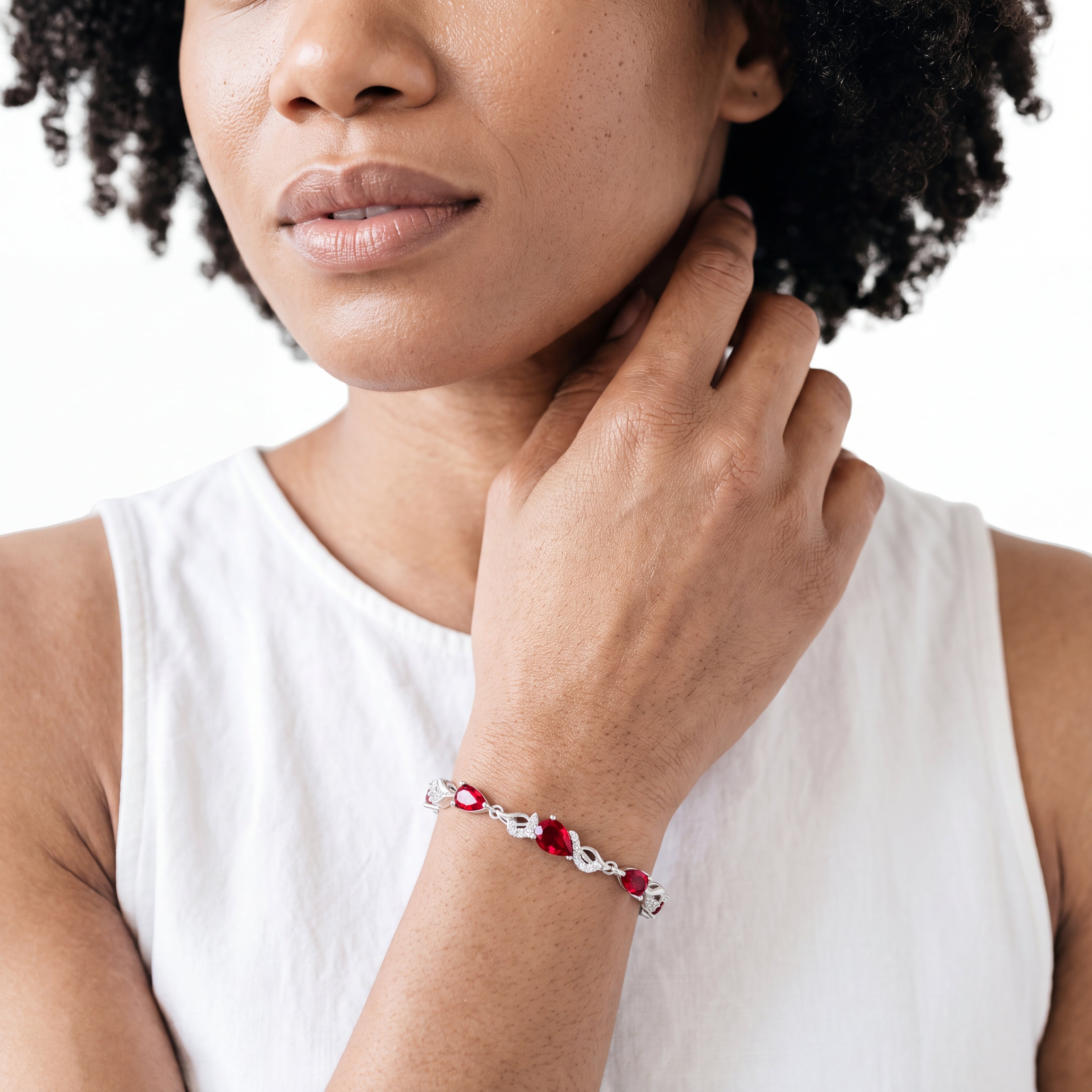 Close-up of a woman wearing the ruby teardrop bracelet on her wrist while touching her neck.