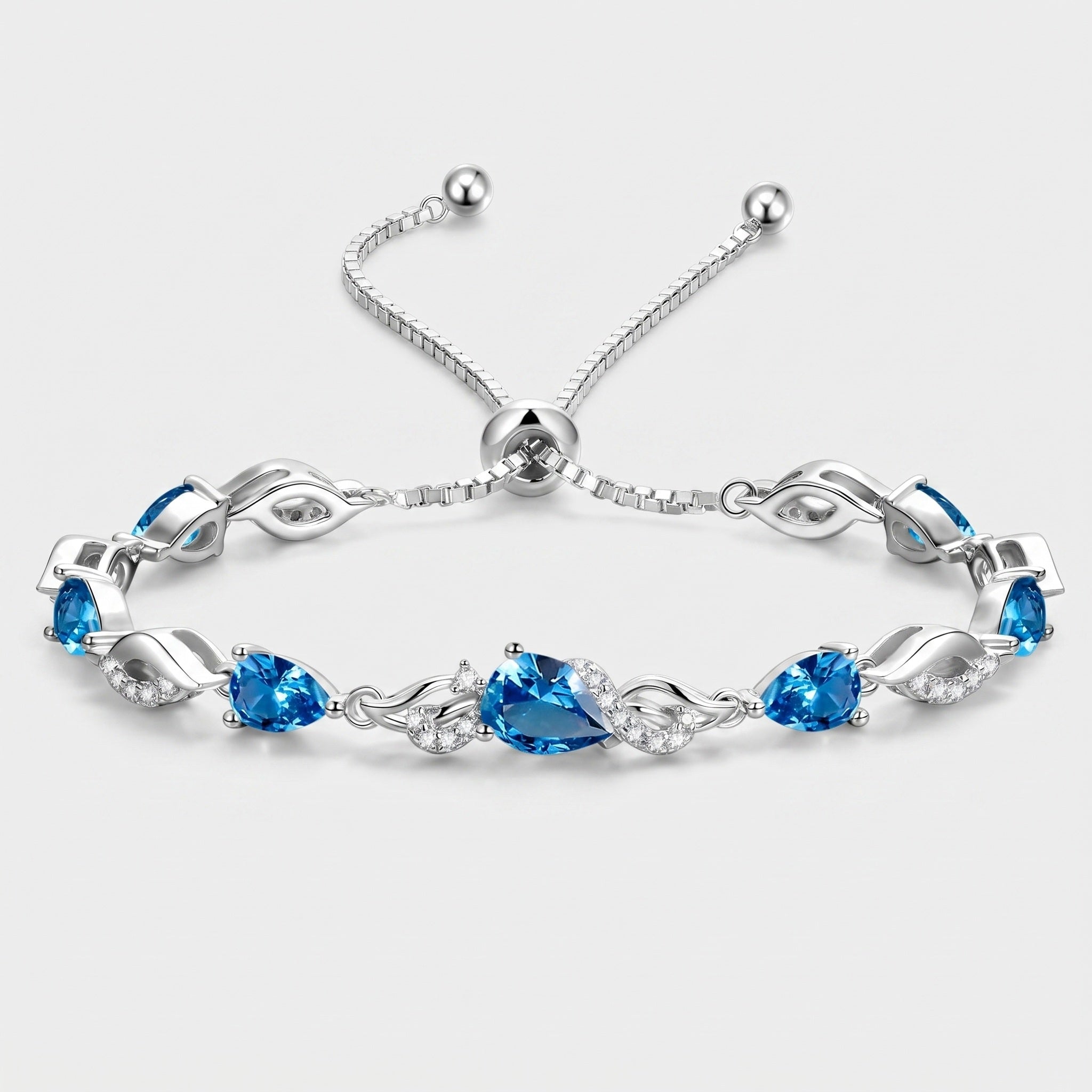 London blue topaz teardrop tennis bracelet in sterling silver laid flat, showing the adjustable bolo clasp and leaf-link design.