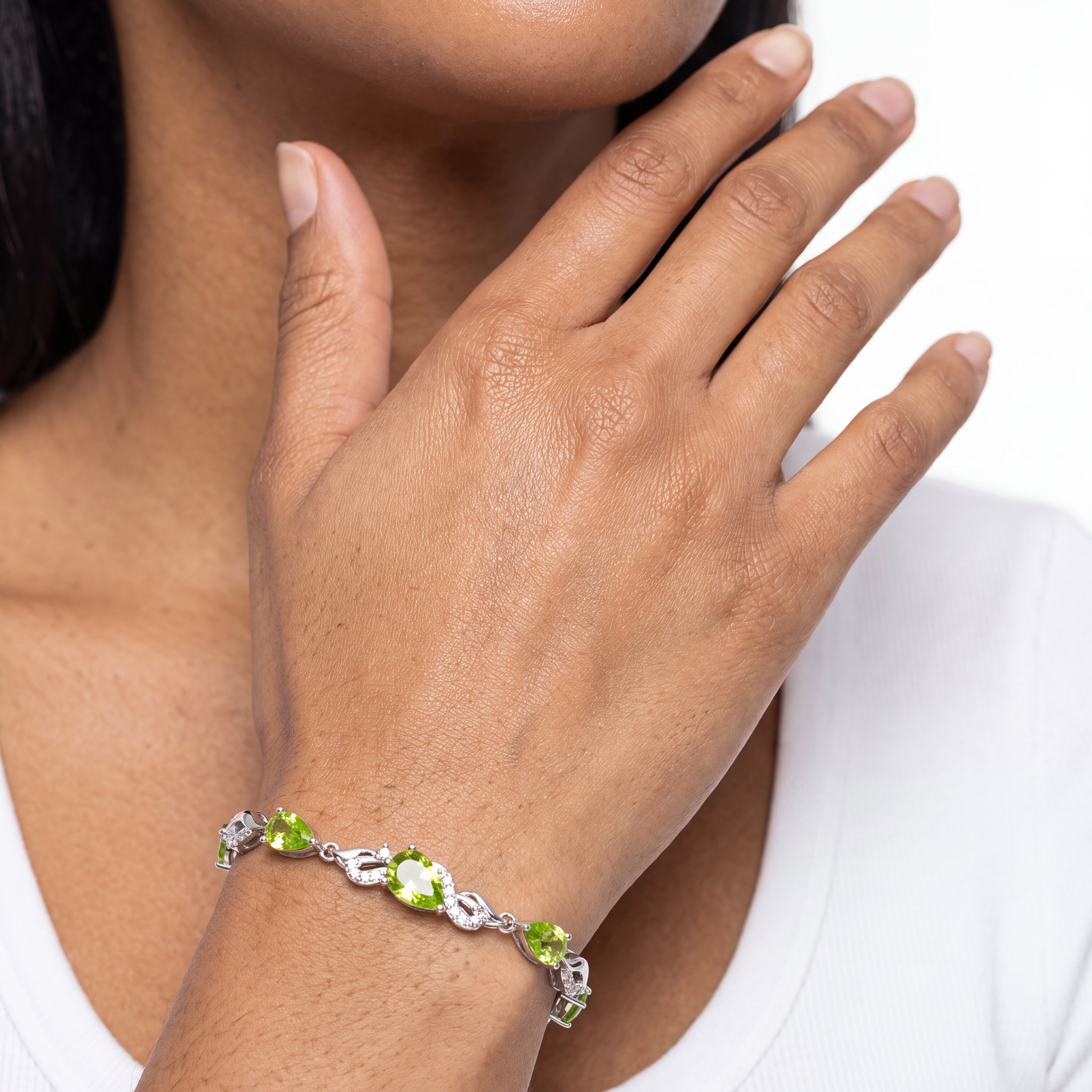 Close-up of the peridot tennis bracelet worn on crossed wrists, showing the bright green teardrop stones.