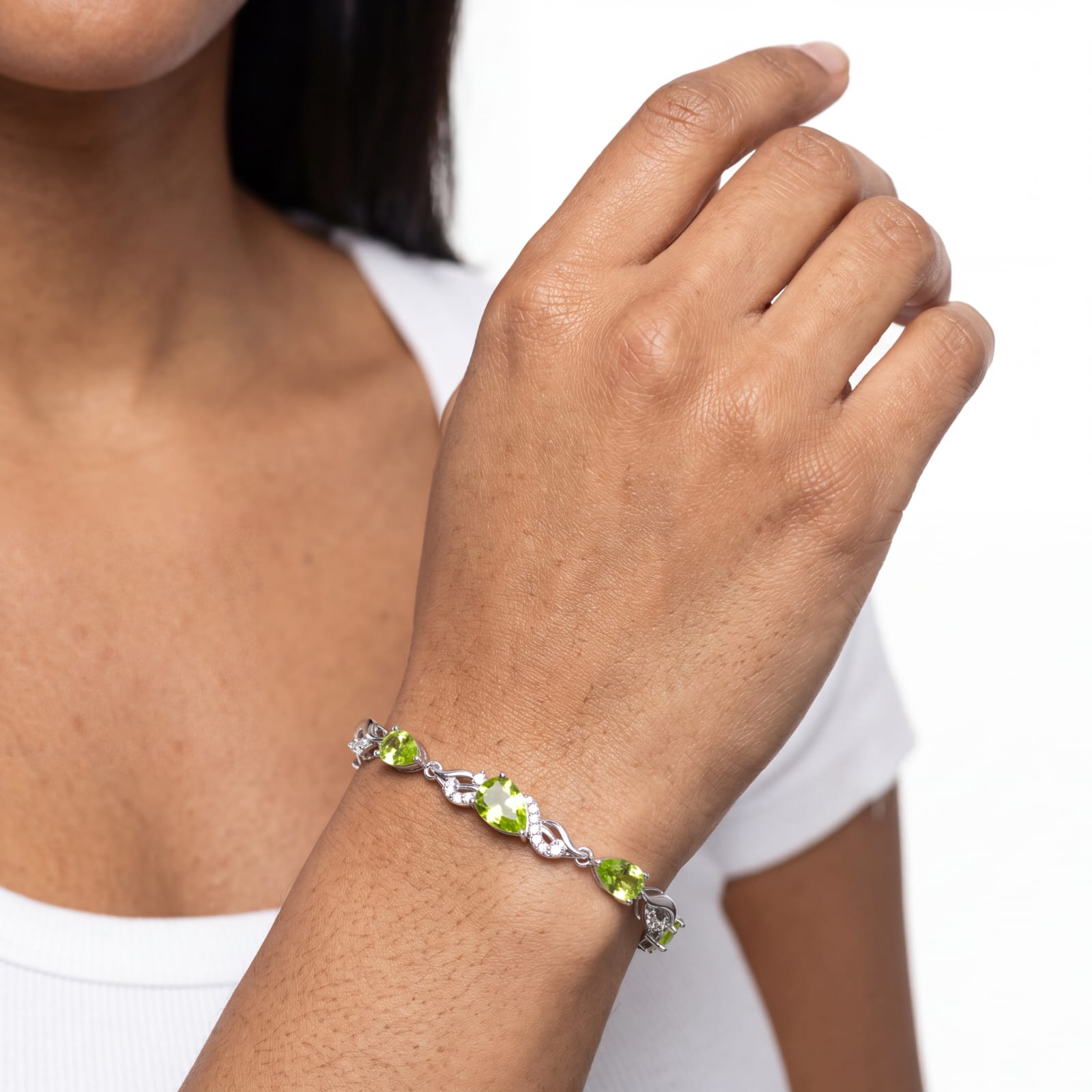 Close-up of the peridot tennis bracelet worn on a raised wrist against a plain background.