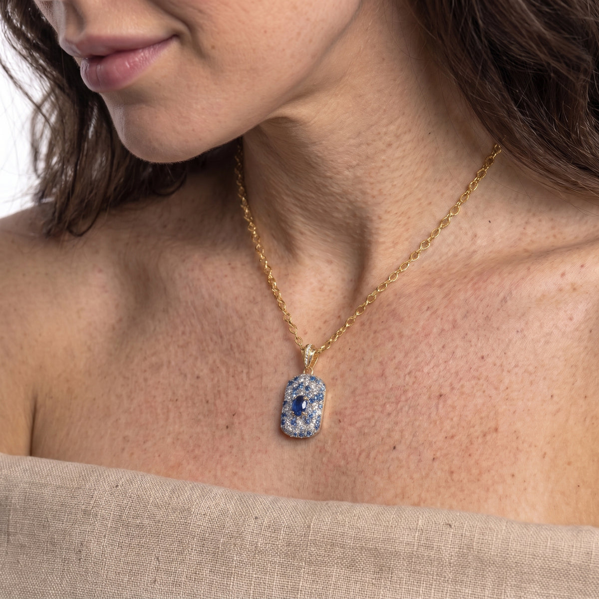 Side view of a sapphire blue pave pendant necklace resting below the collarbone