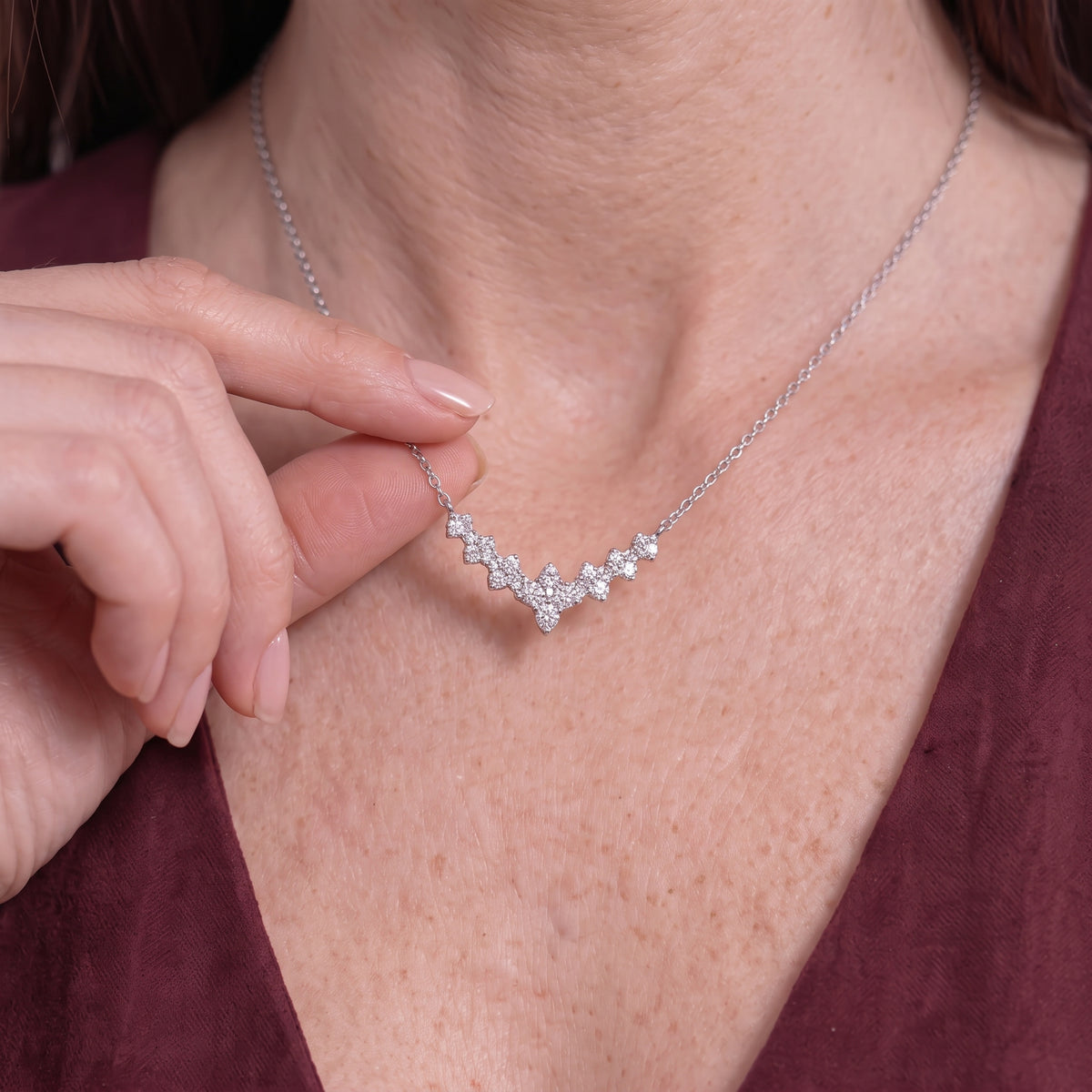Close-up of fingers holding a seven stone moissanite necklace on a thin silver chain