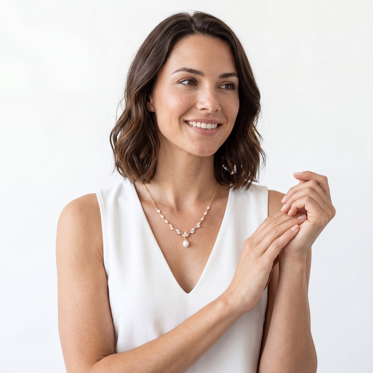Smiling woman in a white V-neck dress wearing a pearl drop CZ bridal necklace