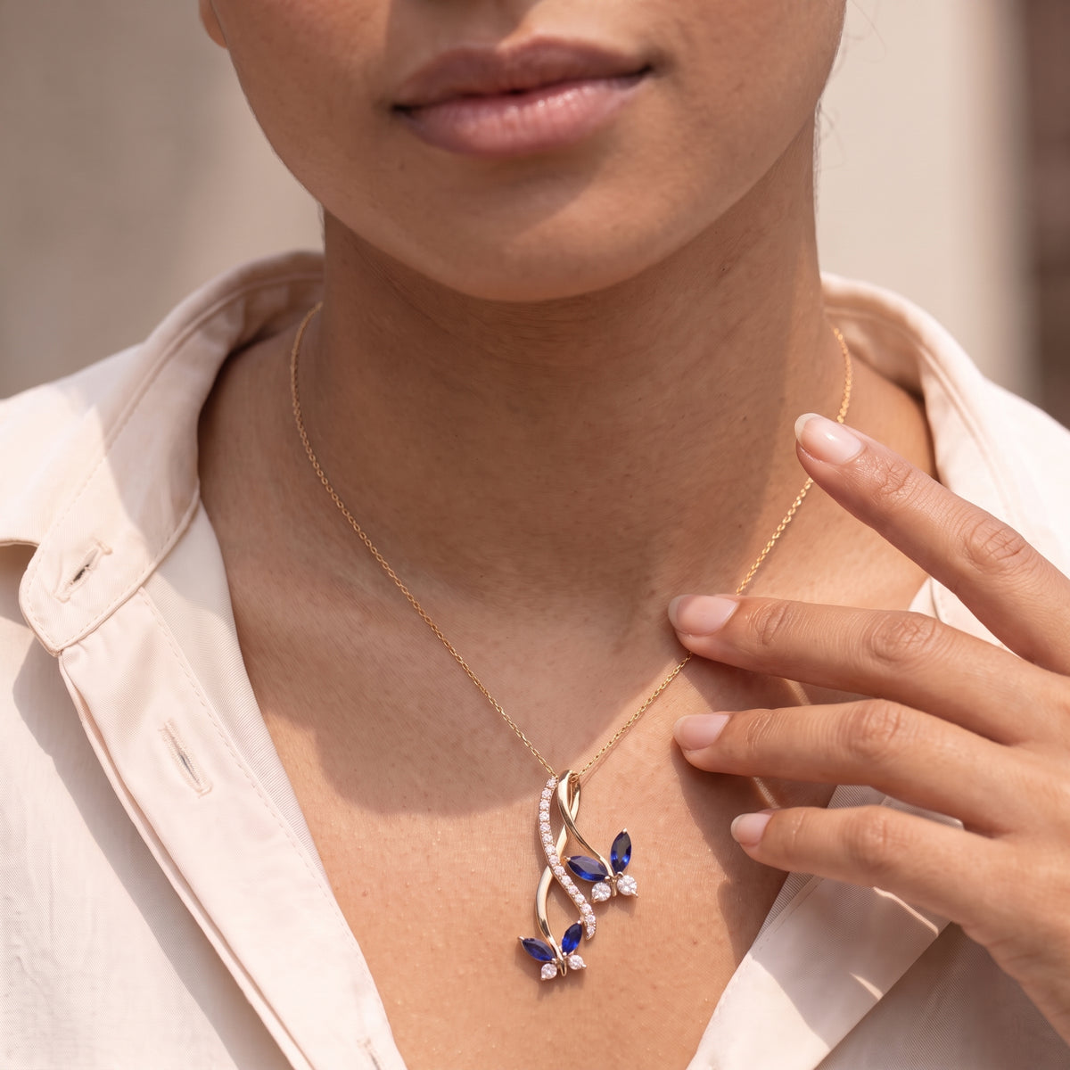 Woman in a blush shirt wearing a blue butterfly infinity pendant on a thin gold chain