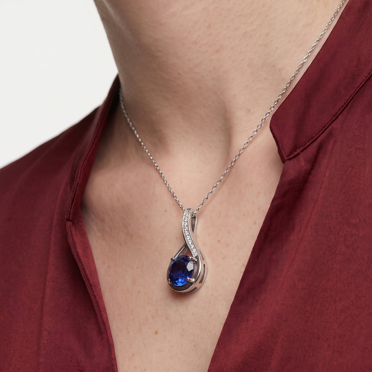 Close-up of a blue sapphire infinity pendant necklace worn with a burgundy blouse