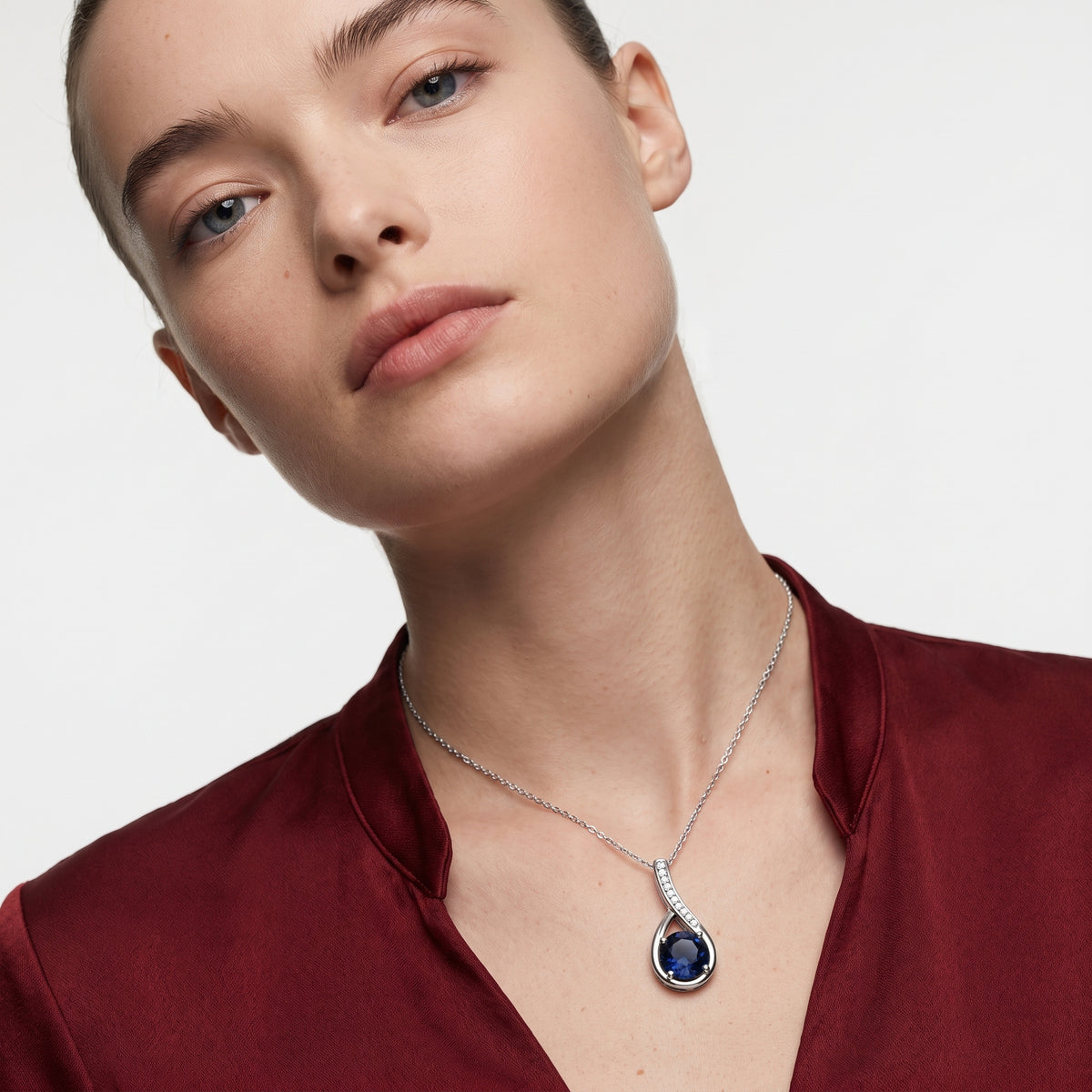 Woman in a burgundy top wearing a blue sapphire and diamond accent silver necklace