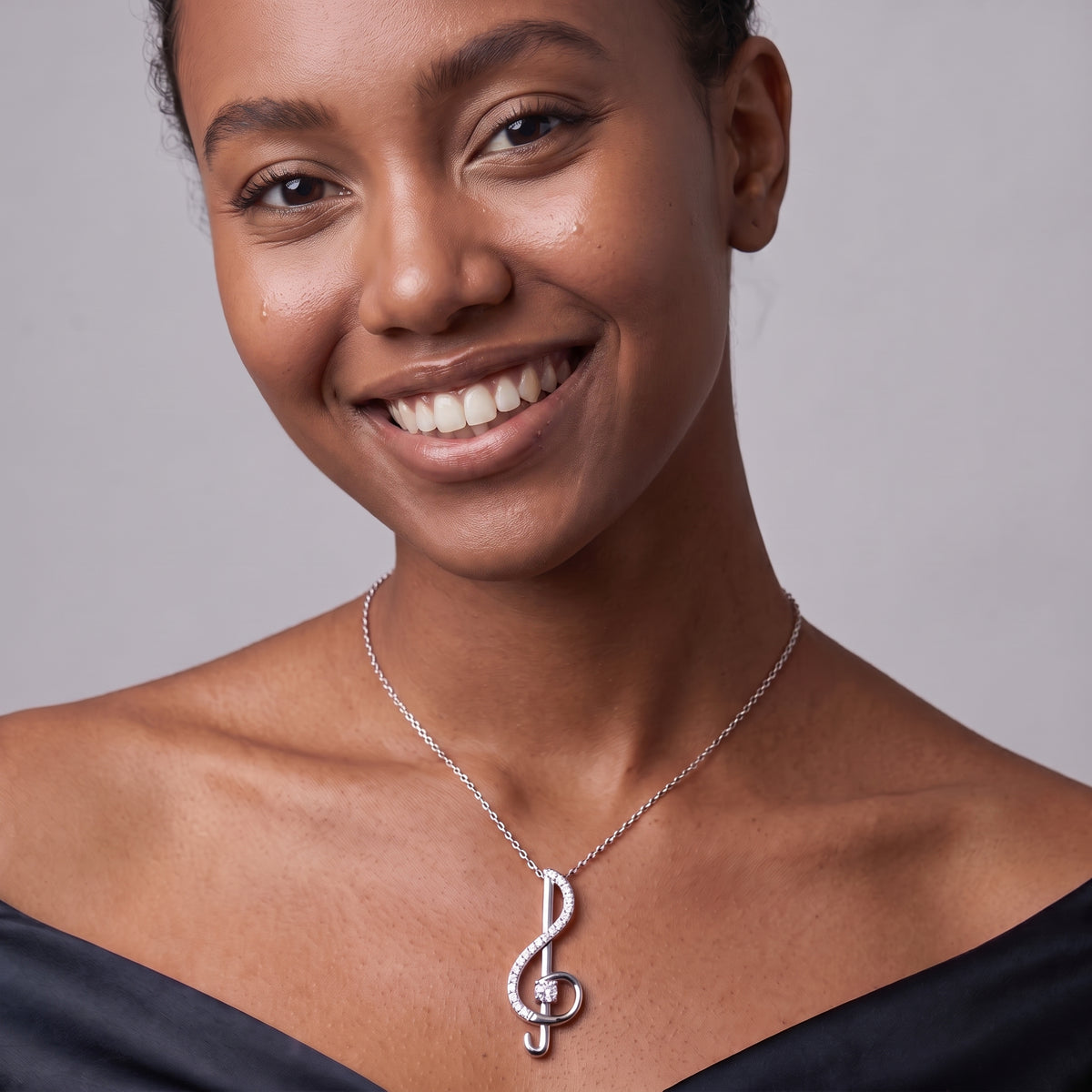 Smiling woman in a black off-shoulder top wearing a silver treble clef music note necklace