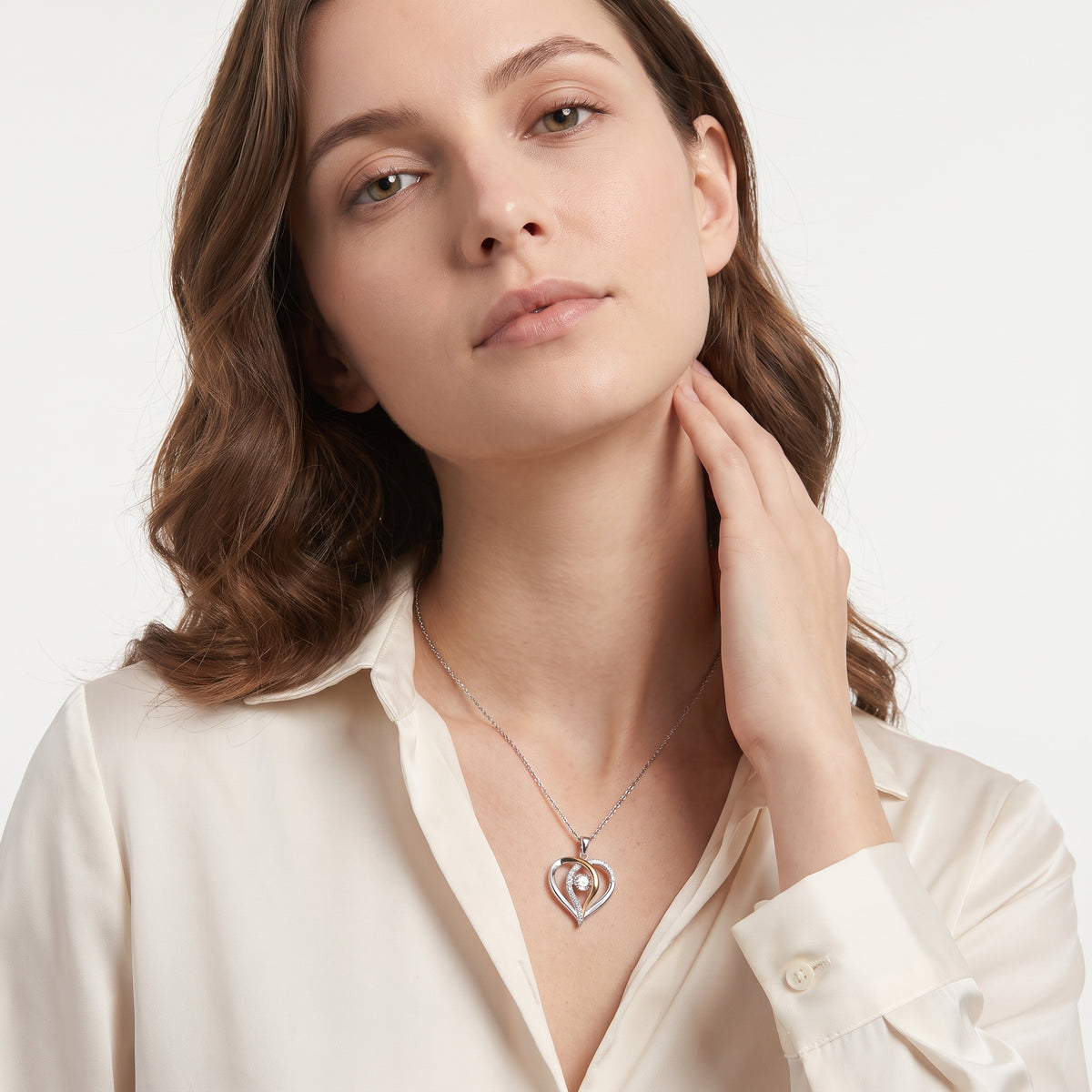 Woman in a cream shirt wearing a two tone moissanite heart necklace, hand at her neck