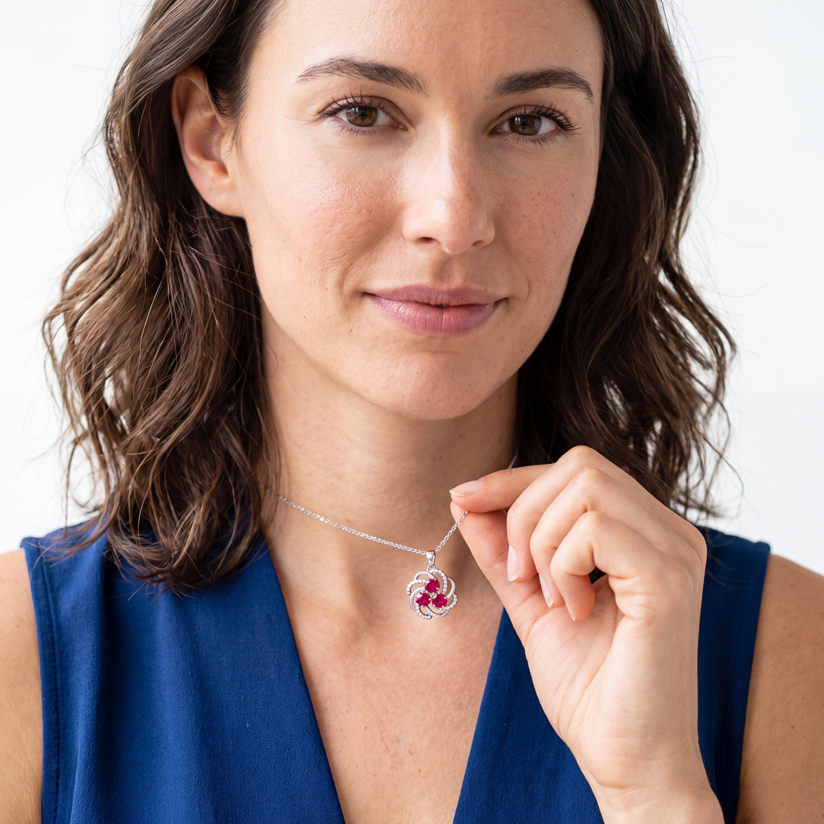 Woman holding a lab created ruby swirl pendant on a thin silver chain